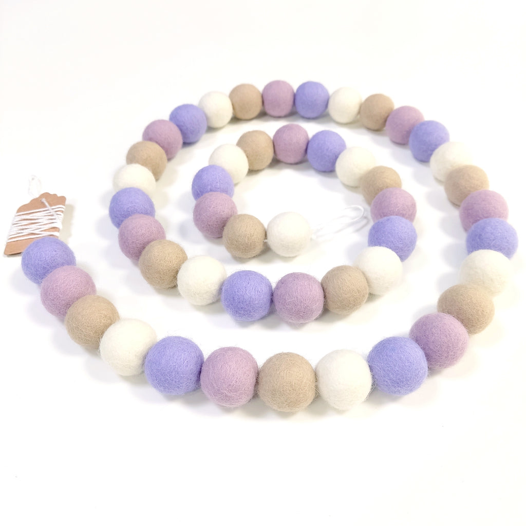 Guirlande de boules de laine feutrée blanc beige mauve disposée en spirale sur une table