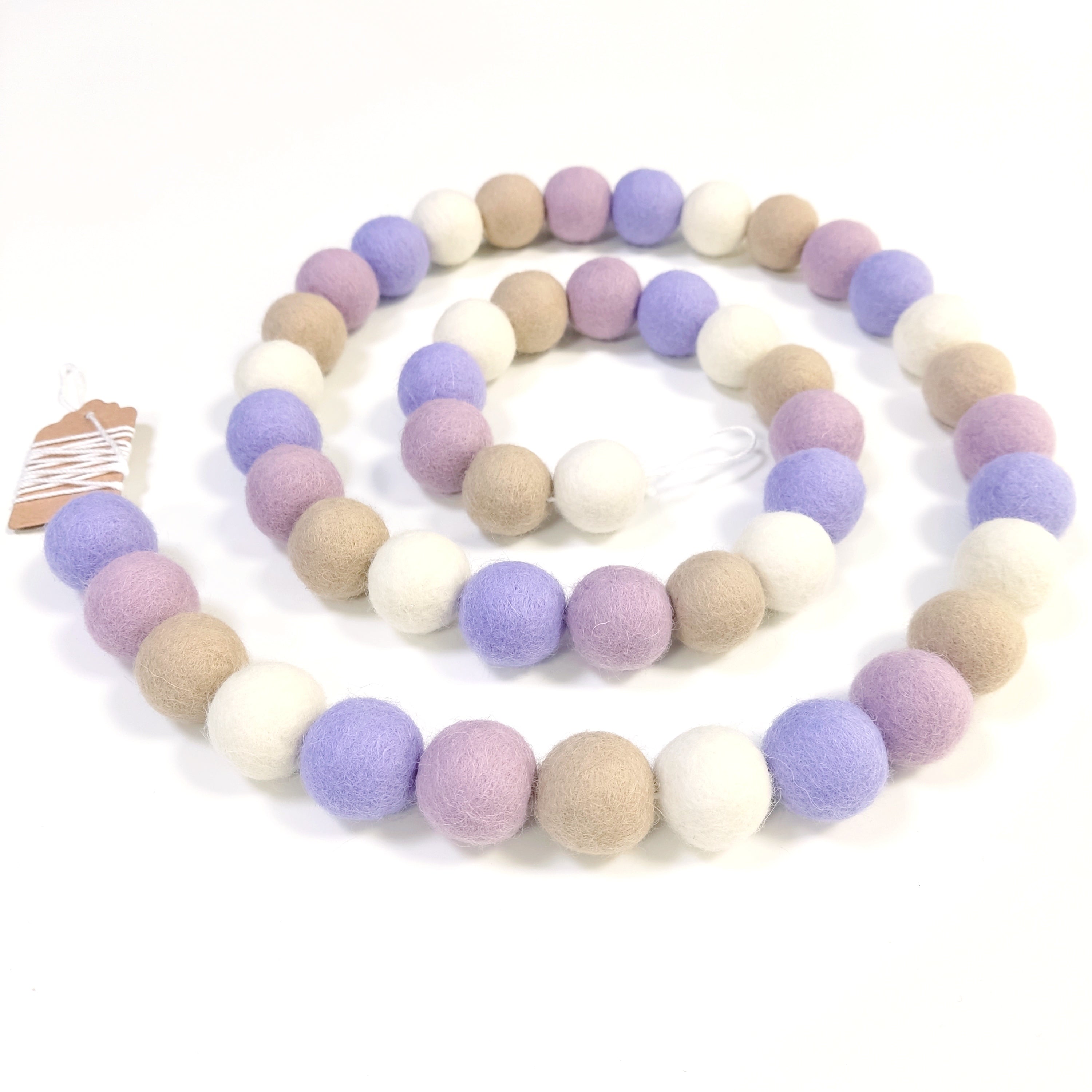 Guirlande de boules de laine feutrée blanc beige mauve disposée en spirale sur une table