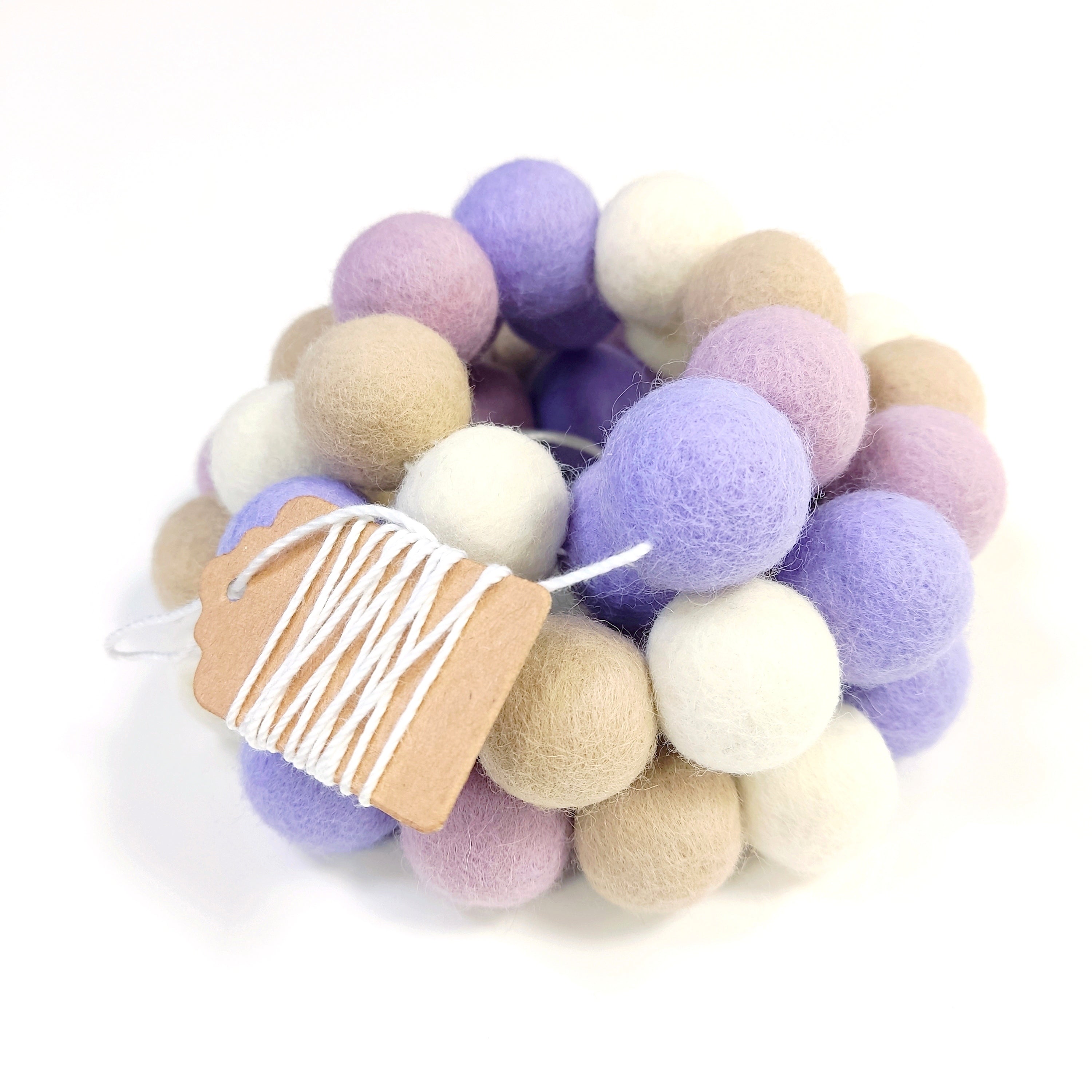 Zoom sur la guirlande de pompons en feutre brume florale aux couleurs blanc beige lilas et lavande avec étiquette