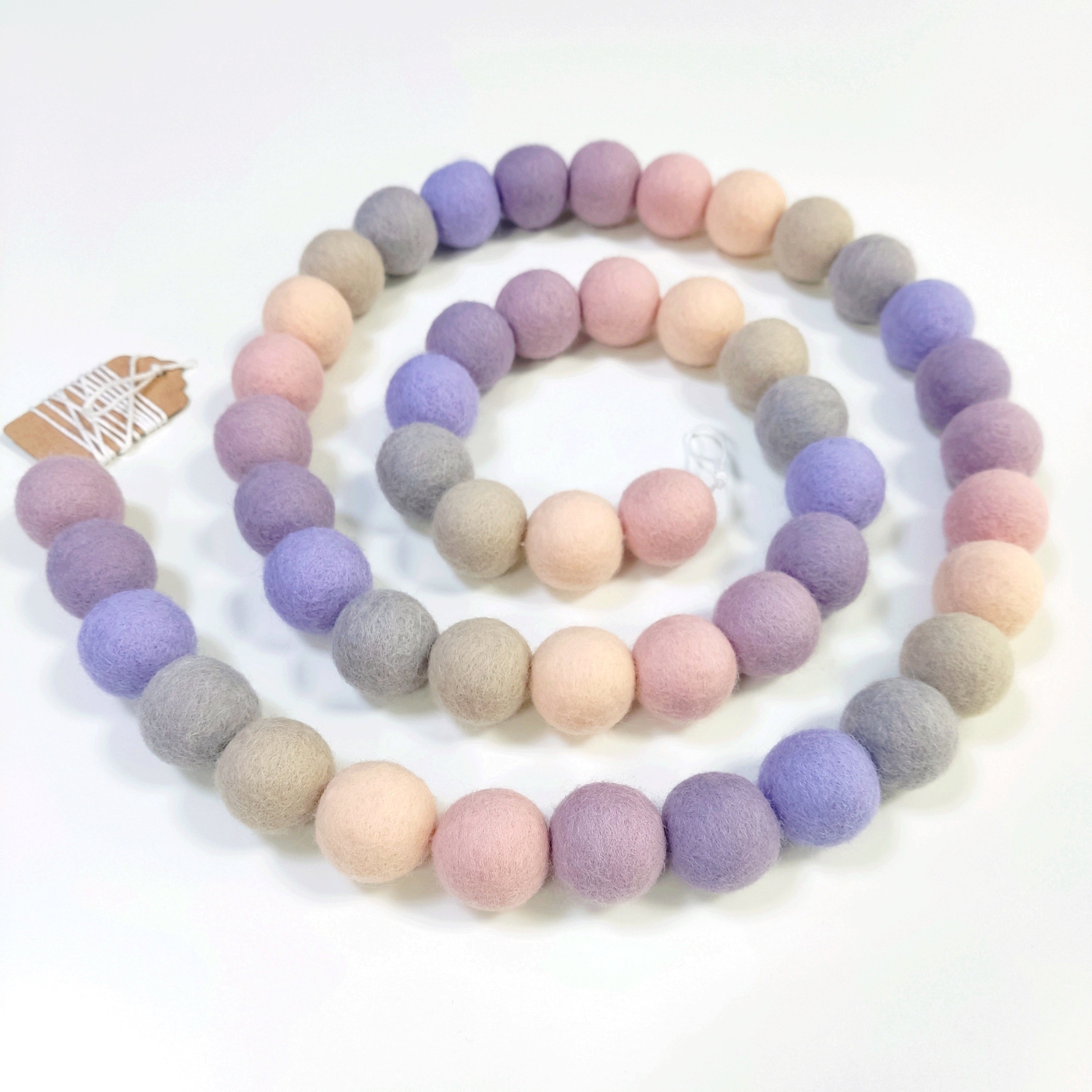 Guirlande en boules de feutre mauve, rose, beige, lilas et lavande, disposée en spirale sur une table