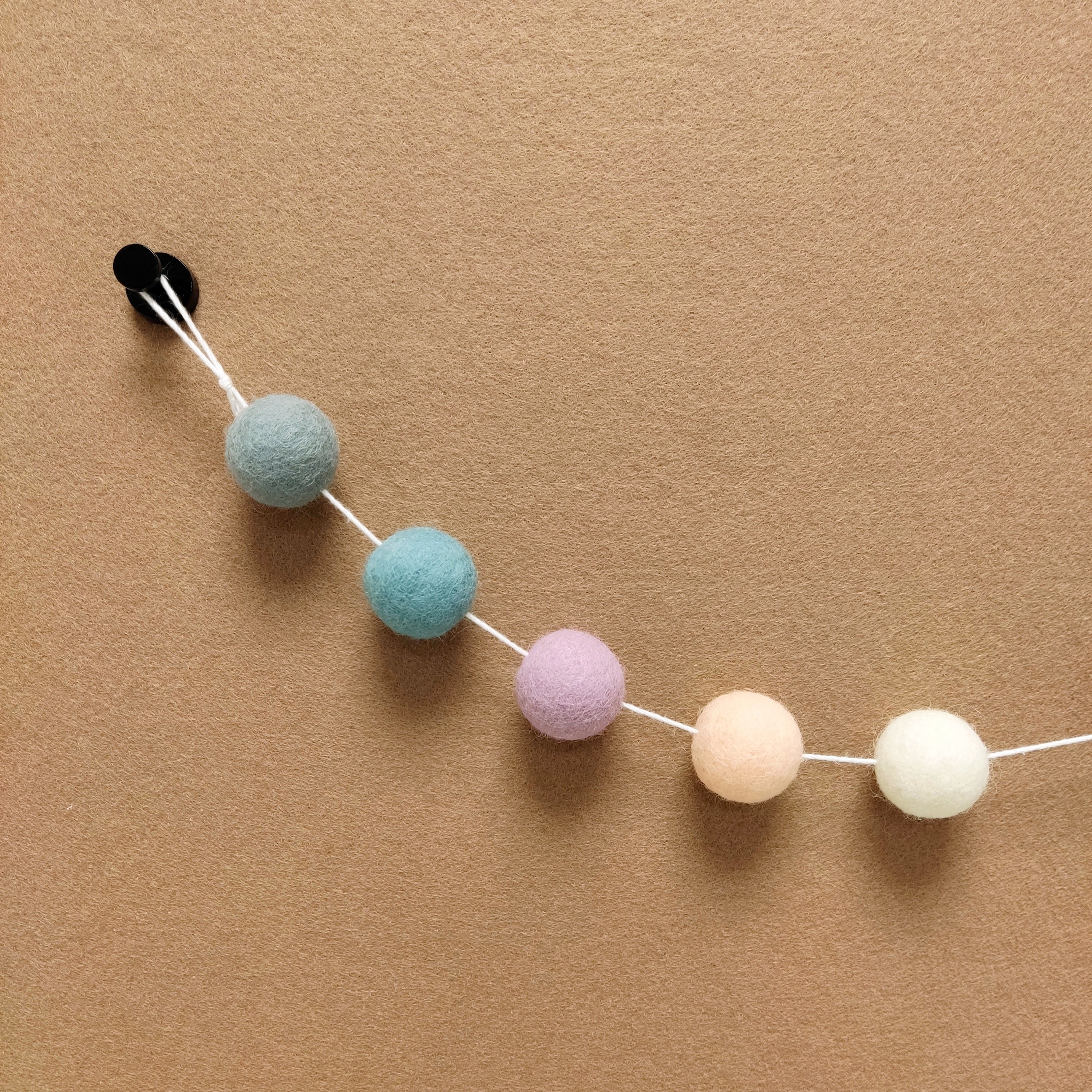 Détails des pompons feutrés de la guirlande brume nordique aux couleurs lilas, blanc, bleu scandinave, beige rosé et gris galet