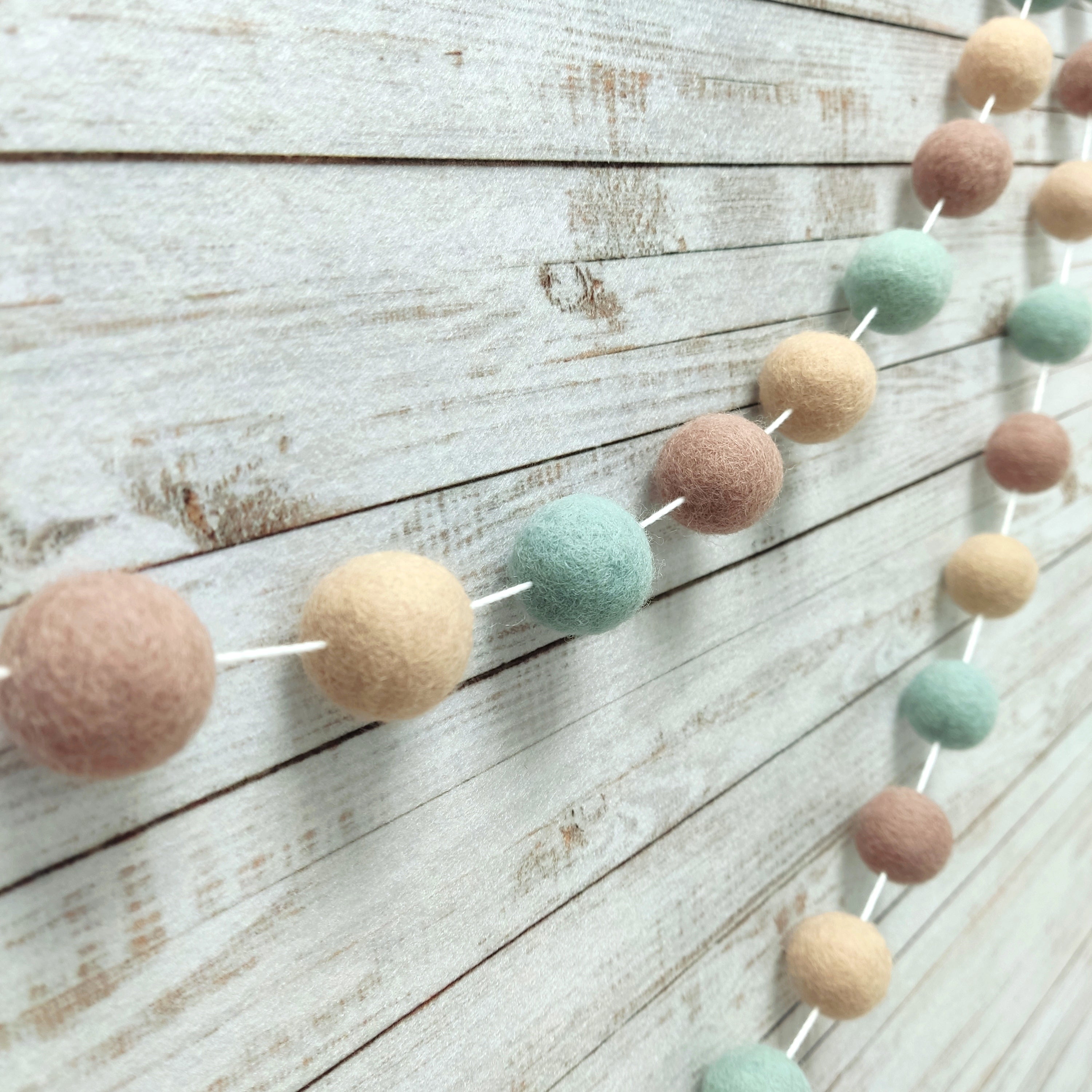 Guirlande en boules de feutre céladon et beige vue de profil sur le mur