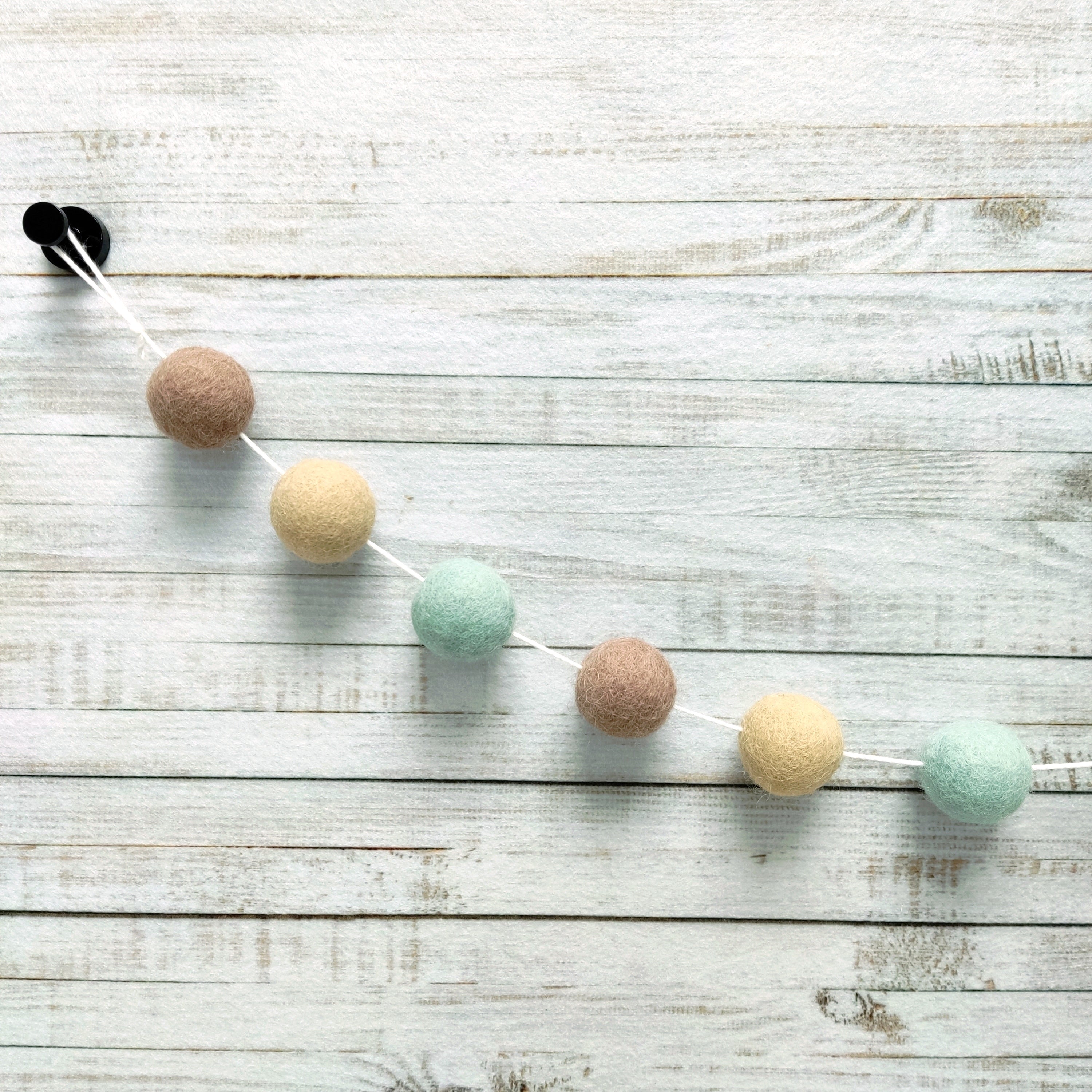 Zoom sur les pompons de feutre de la guirlande vert céladon, beige poudré et beige cappuccino