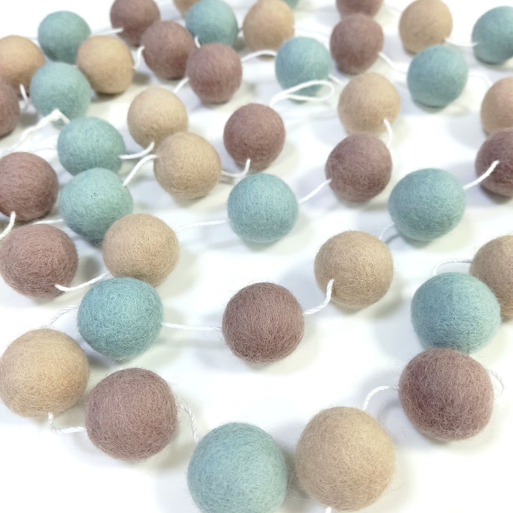 Guirlande de pompons en feutre de laine mérinos posée sur une table avec le pompons espacés