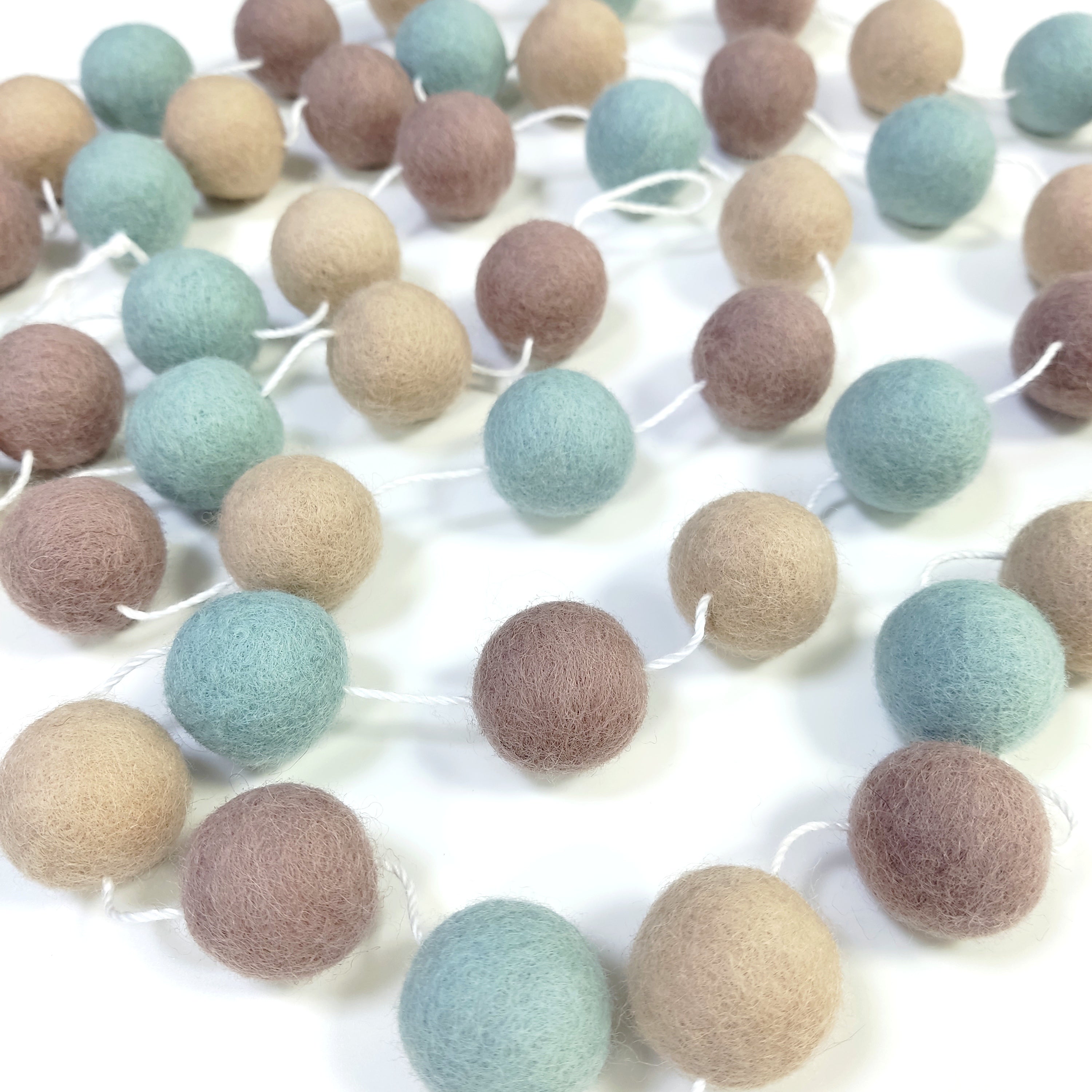 Guirlande de pompons en feutre de laine mérinos posée sur une table avec le pompons espacés