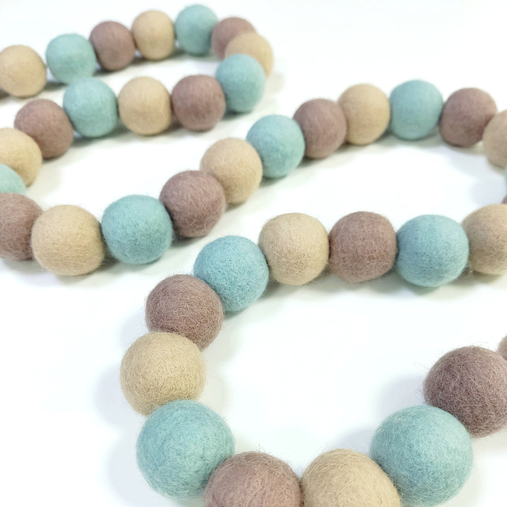 Guirlande de boules de feutre vert céladon, beige et cappuccino disposée en serpentin sur une table