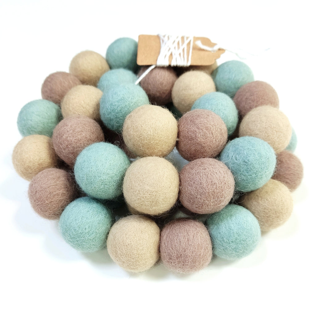 Zoom sur la guirlande de pompons feutrés céladon beige avec étiquette