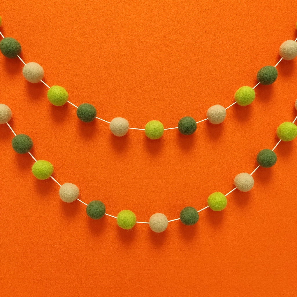 Guirlande en boules de feutres pour décoration bohème vert beige  sur un mur