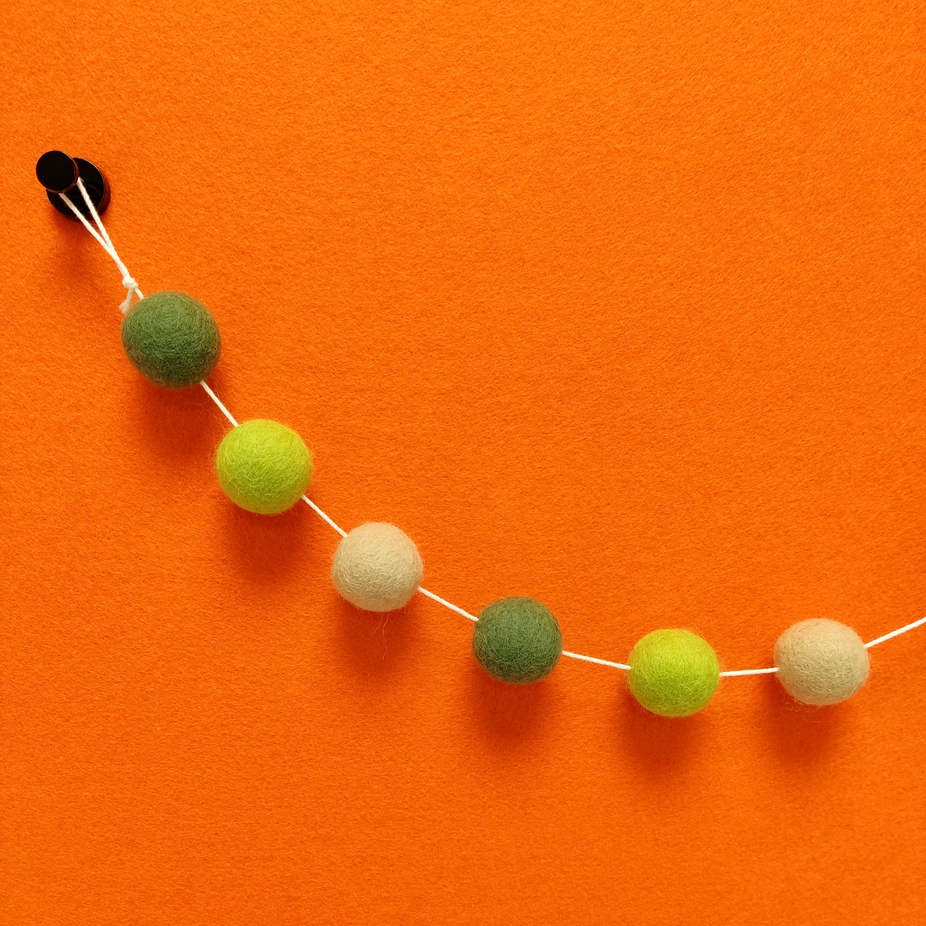 Zoom sur les pompons de feutre de la guirlande vert citron, vert matcha et beige poudré.
