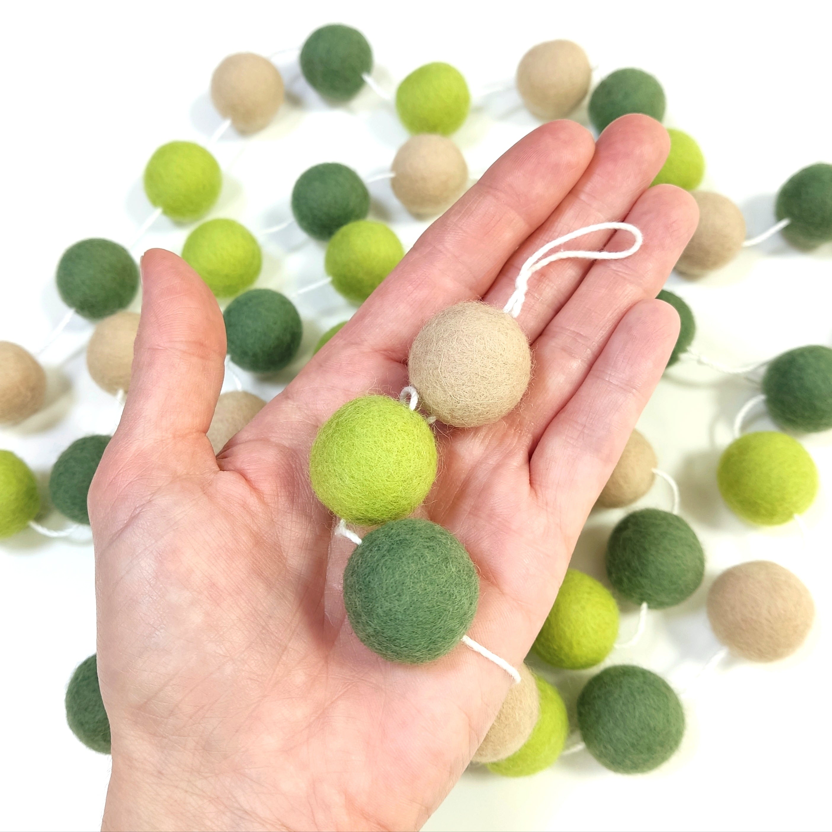 Pompons feutrés de 2,5 cm de la guirlande vert et beige dans une main
