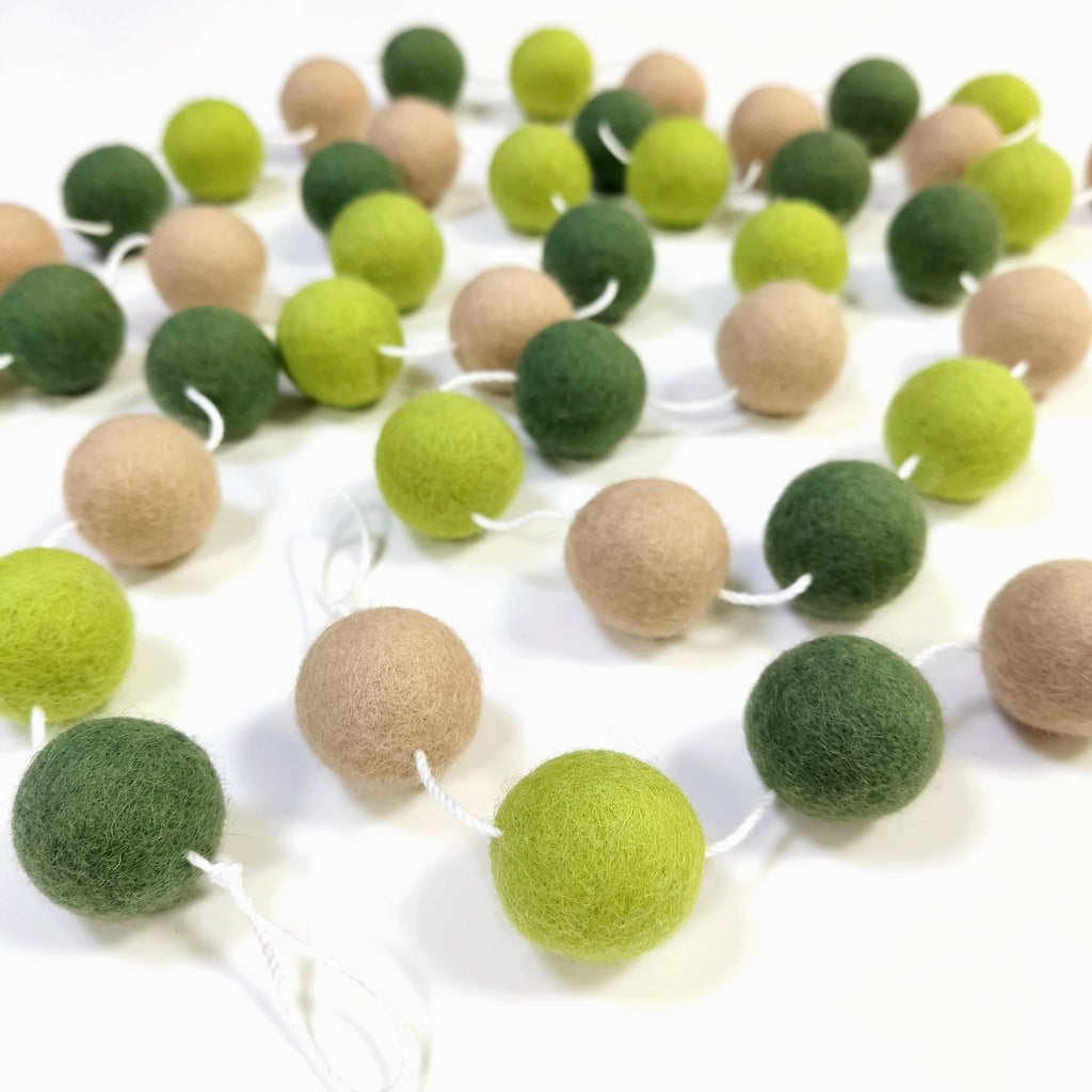 Guirlandes de boules de feutres vert citron, vert matcha et beige poudré, étalée sur une table avec les pompons espacés