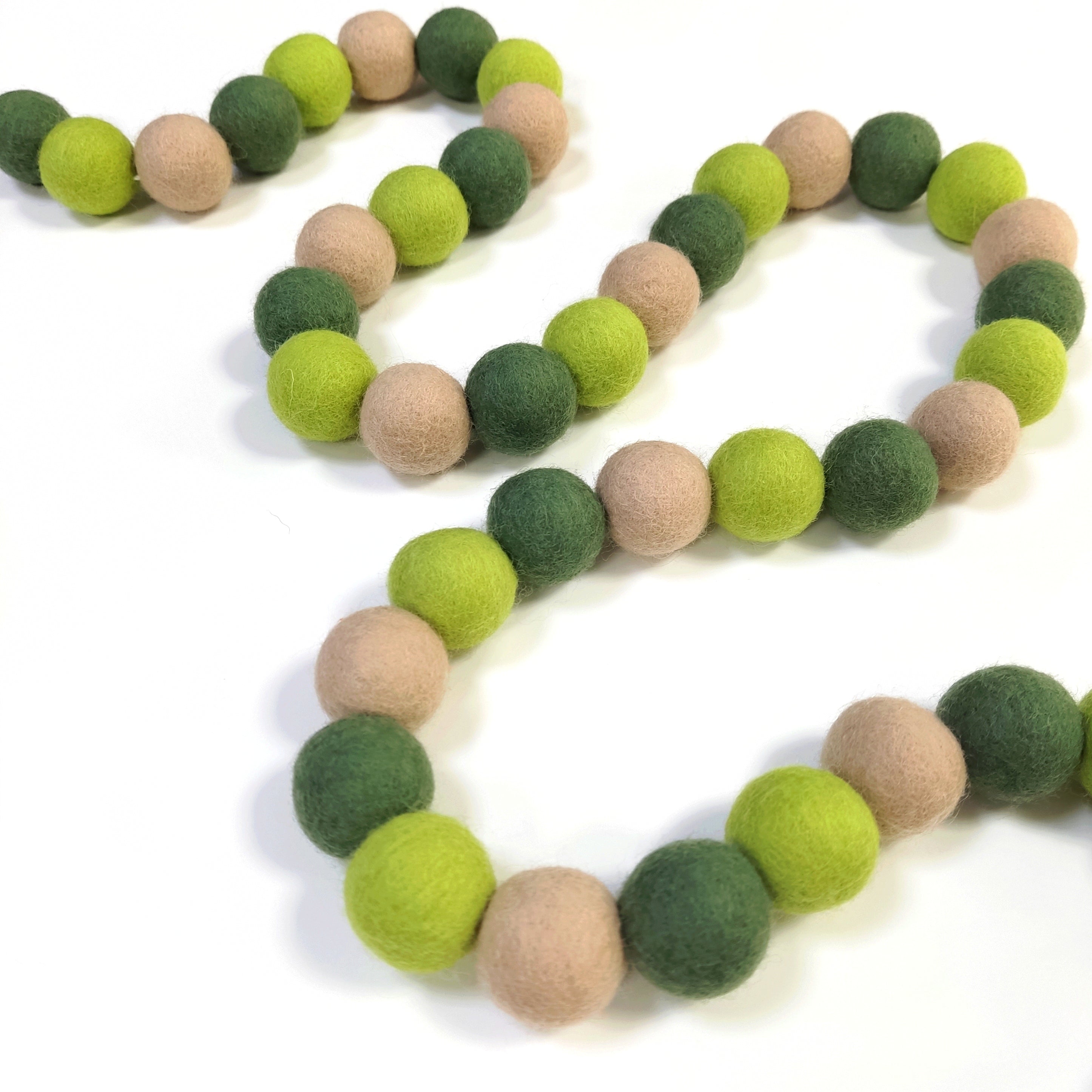 Guirlande de pompons vert et beige en serpentin sur une table avec les boules de feutre non-espacées