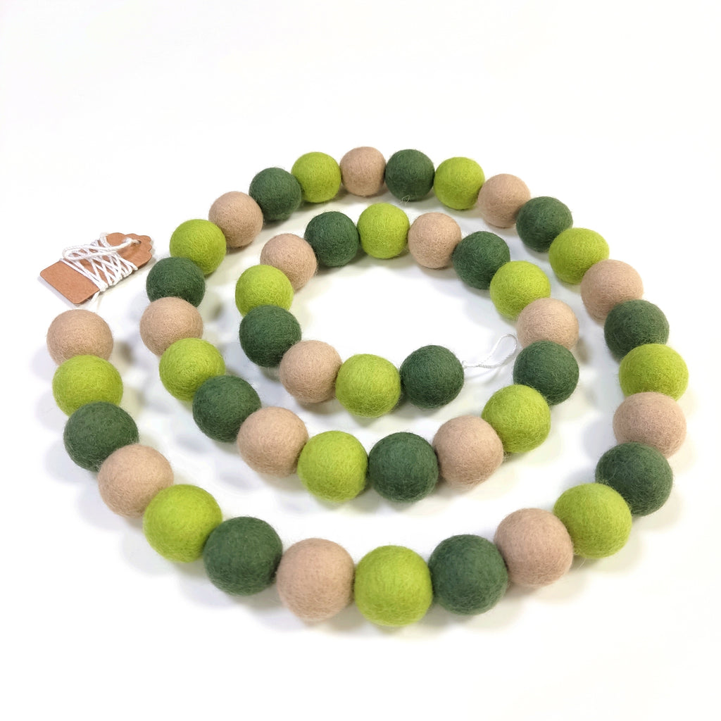 Guirlande teintes verte et beige disposée en spirale sur une table avec les pompons resserrés sur le fil