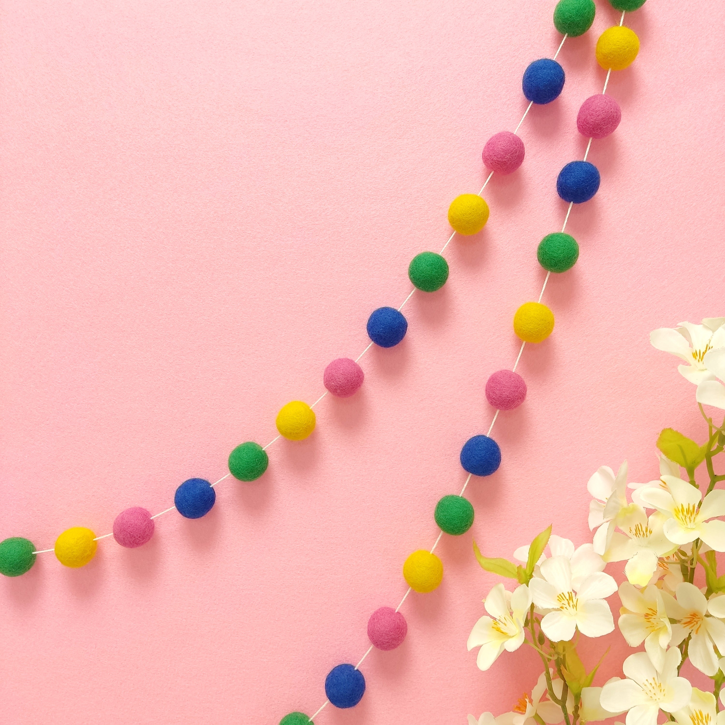 Guirlande de pompons en laine mérinos confettis fixée en arc de cercle sur un mur, faite main en France
