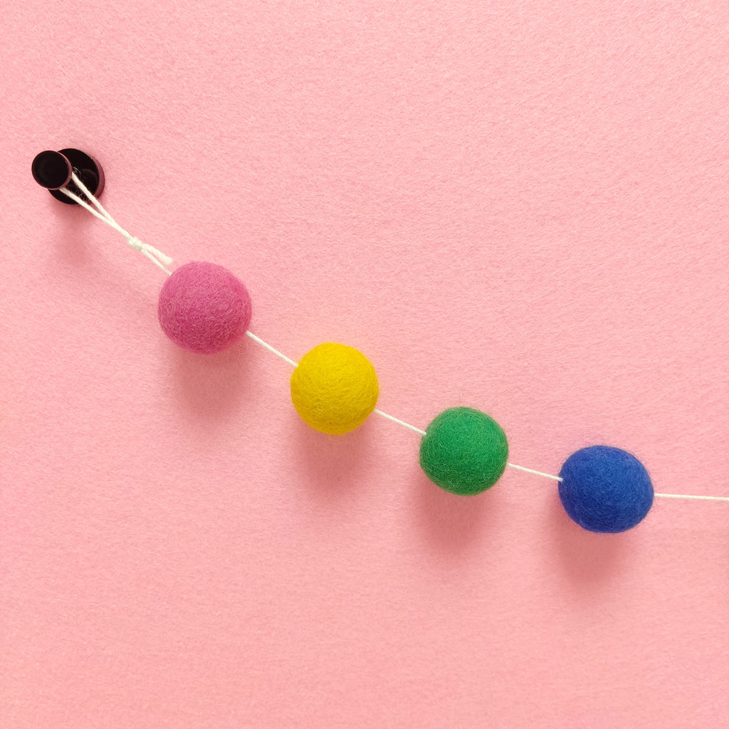 Détail des 4 couleurs de pompons feutrés bleu indigo, vert prairie, jaune soleil et rose bonbon de la guirlande Confettis