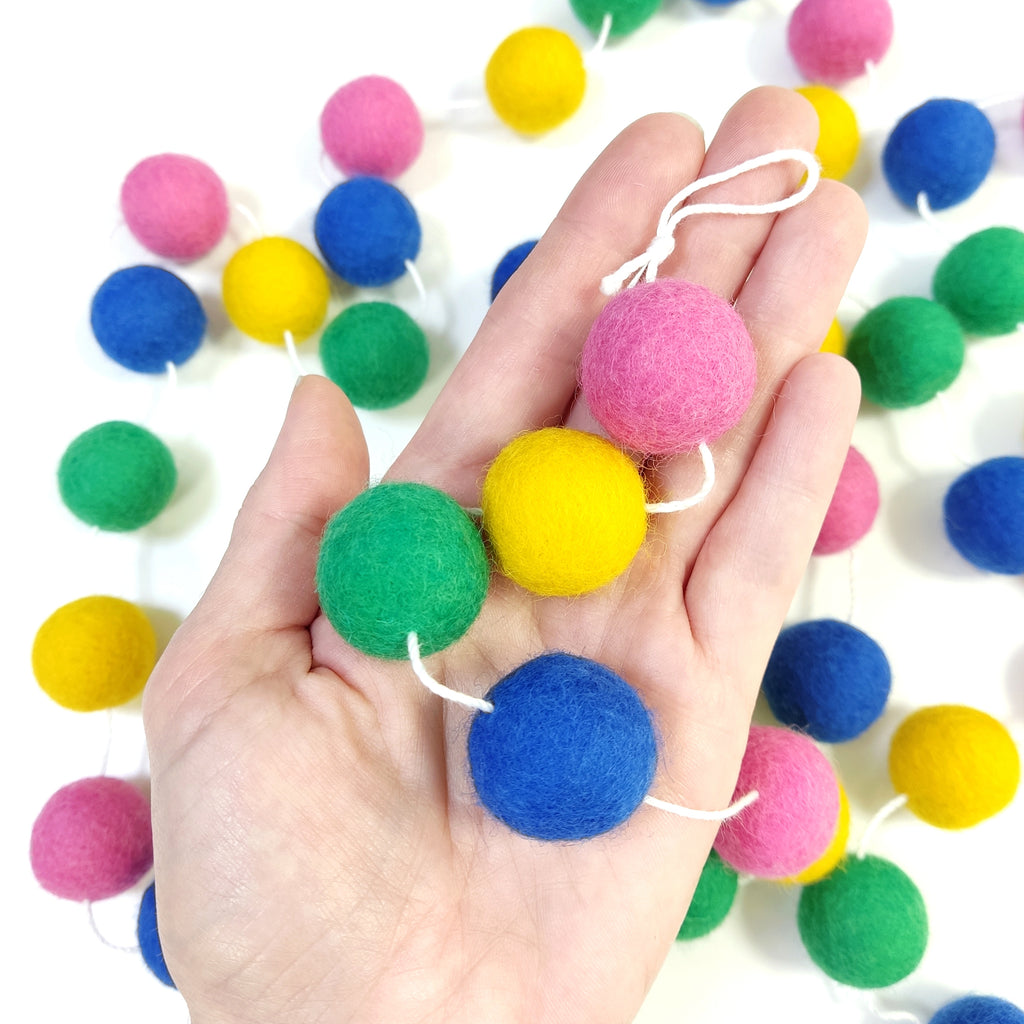 Zoom sur les pompons en laine mérinos confettis dans une main, teintes vives et festives