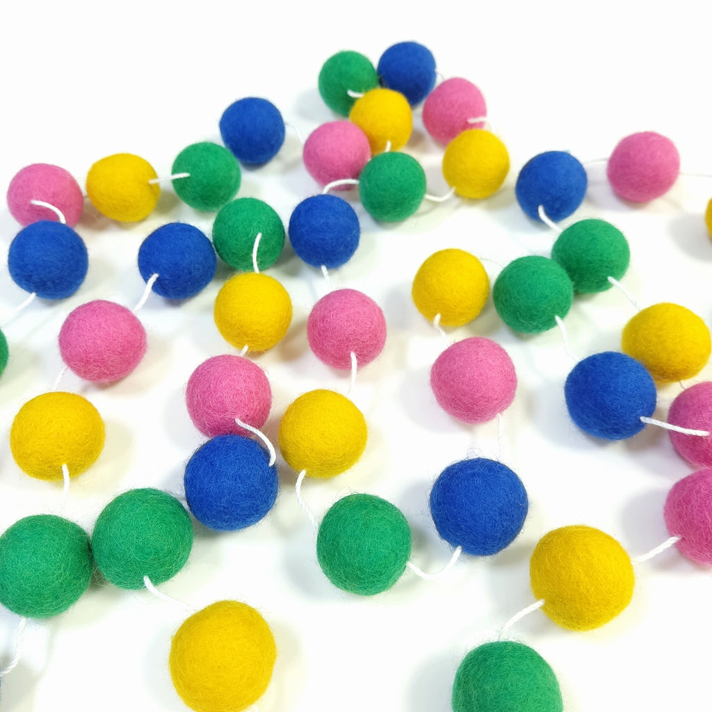 Guirlande de pompons feutrés confettis étalée sur une table avec les pompons espacés sur le fil