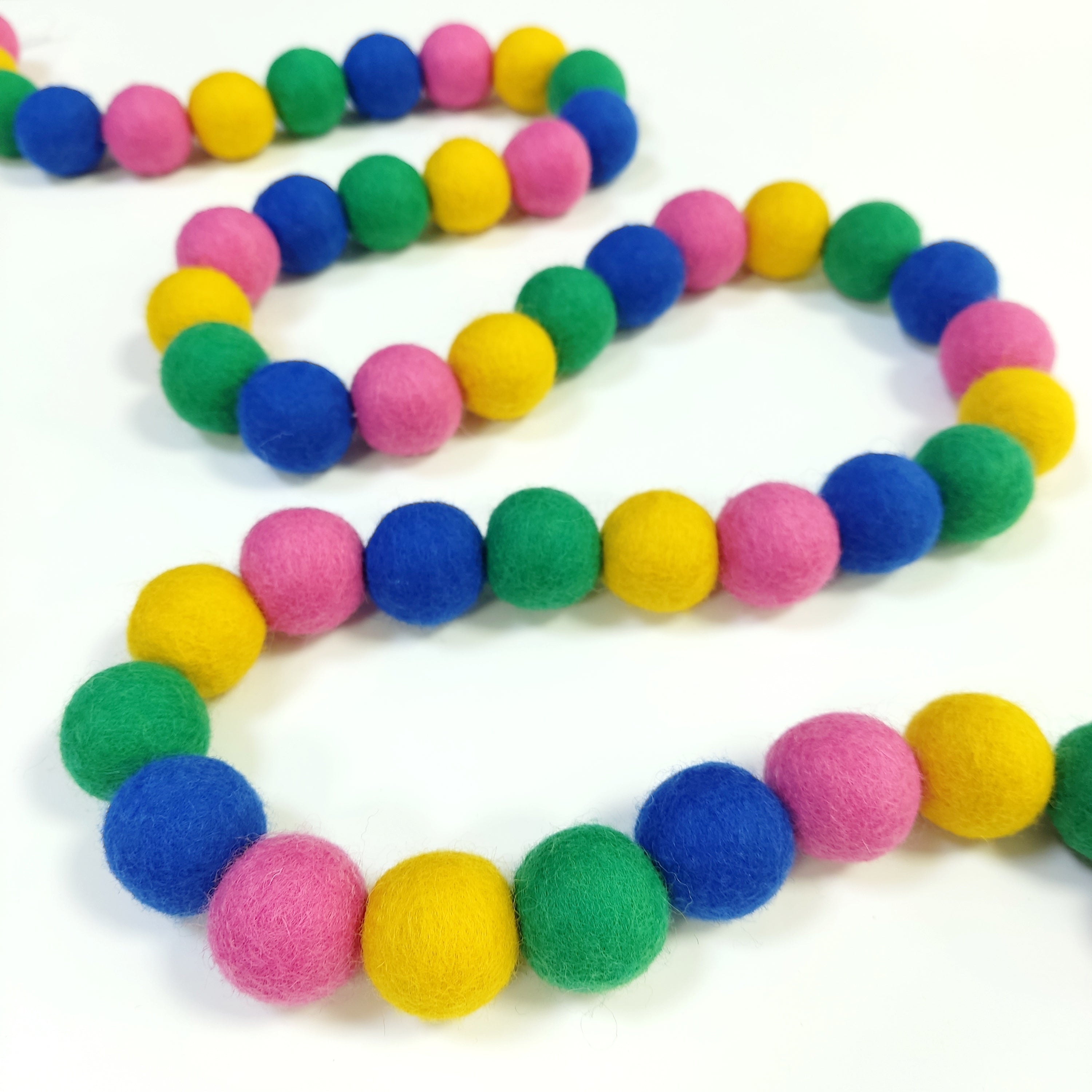 Guirlande en boules de feutre confettis disposée en serpentin sur une table