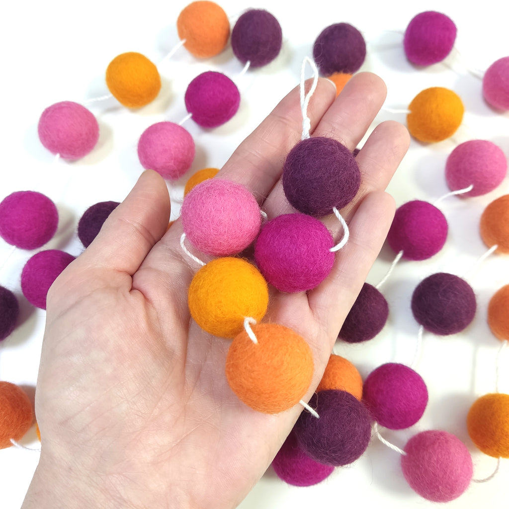 Détail des pompons de laine feutrée de la guirlande dahlias rose et orange dans une main