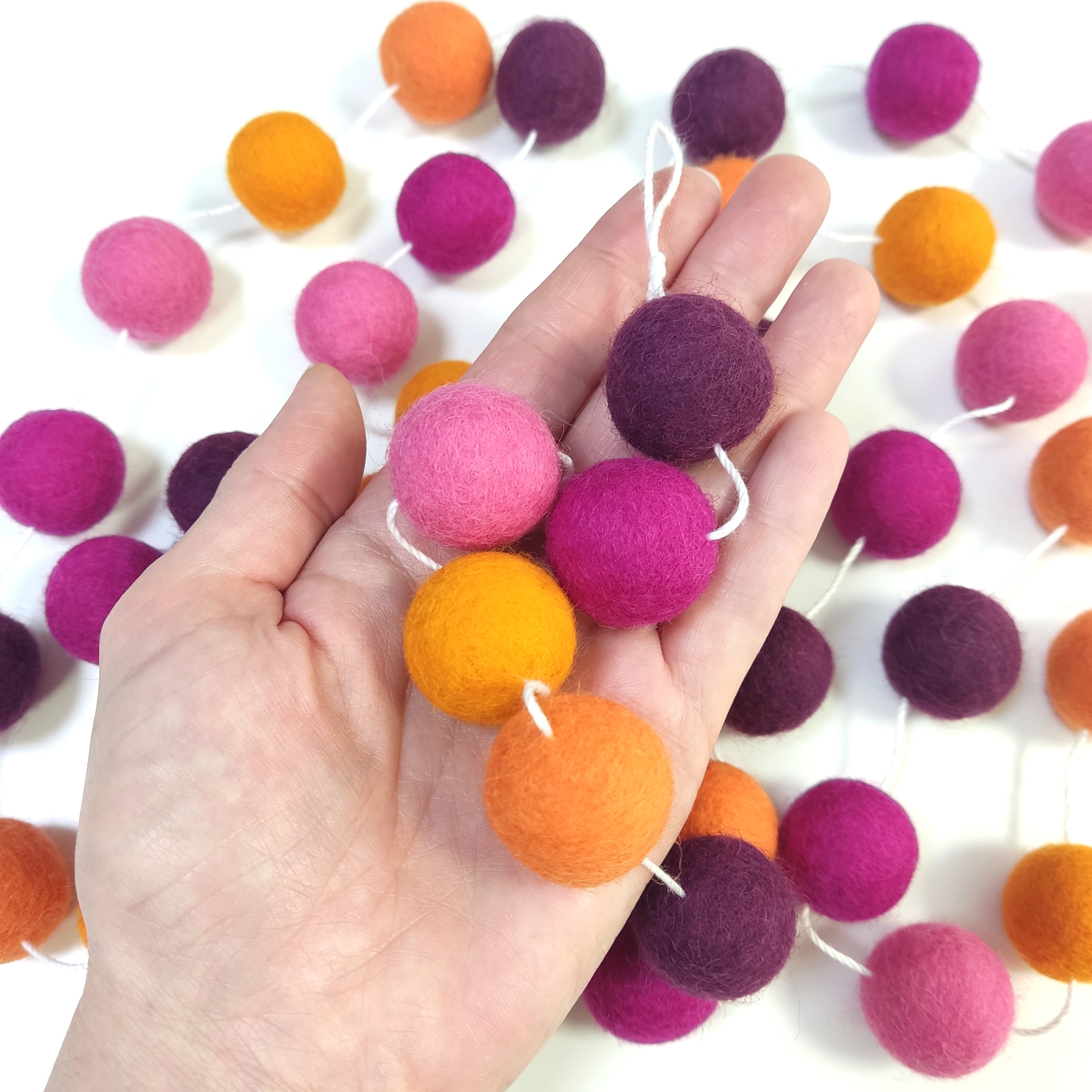 Détail des pompons de laine feutrée de la guirlande dahlias rose et orange dans une main