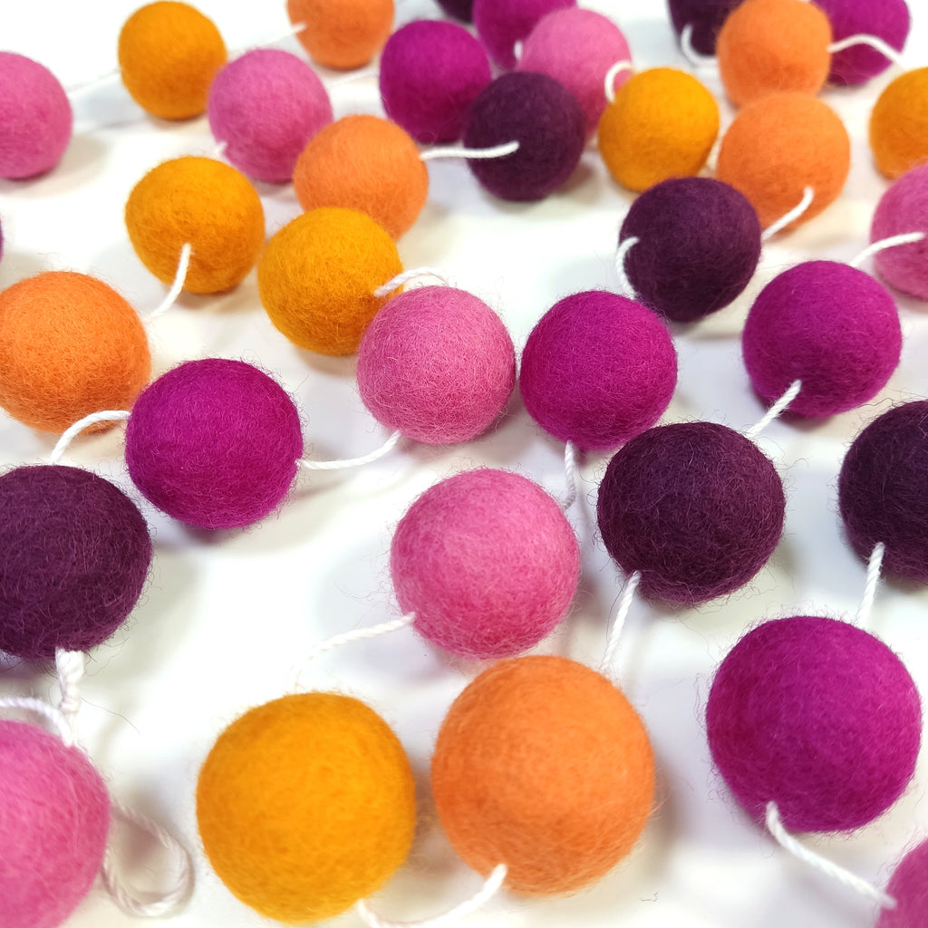 Guirlande de pompons dahlias aux teintes rose et orange étalée sur une table