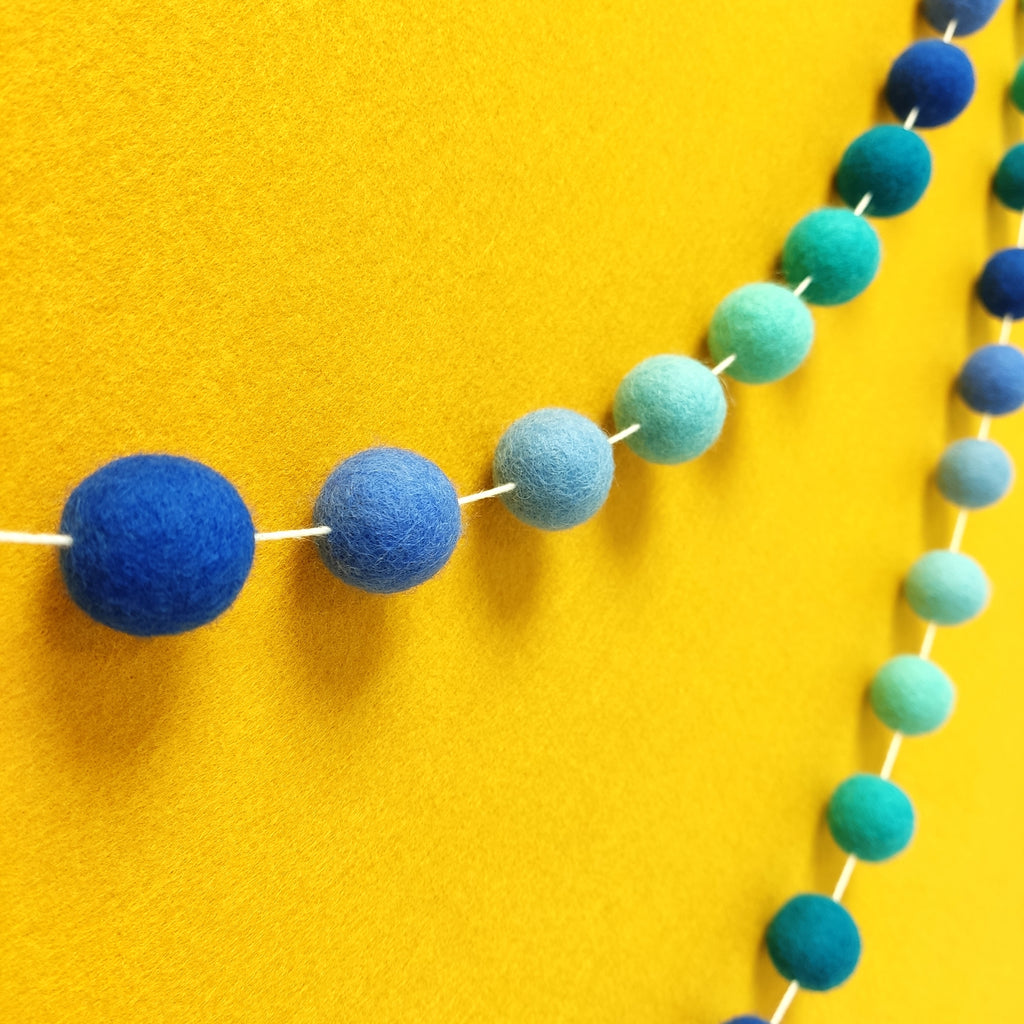 Guirlande en boules de feutre indigo et bleu turquoise vue de profil sur un mur
