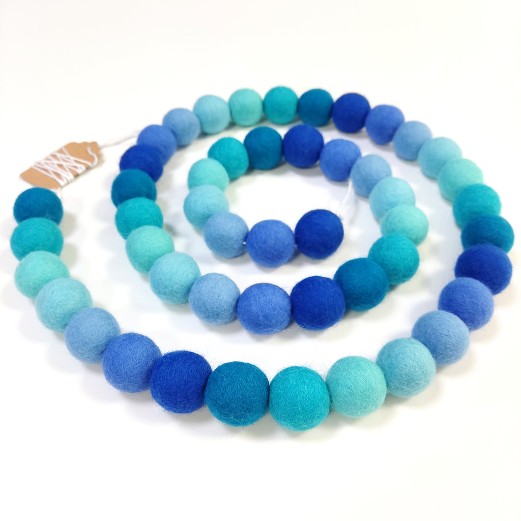 Guirlande de boules de laine feutrée aux teintes bleues disposée en spirale avec les pompons rassemblés sur le fil