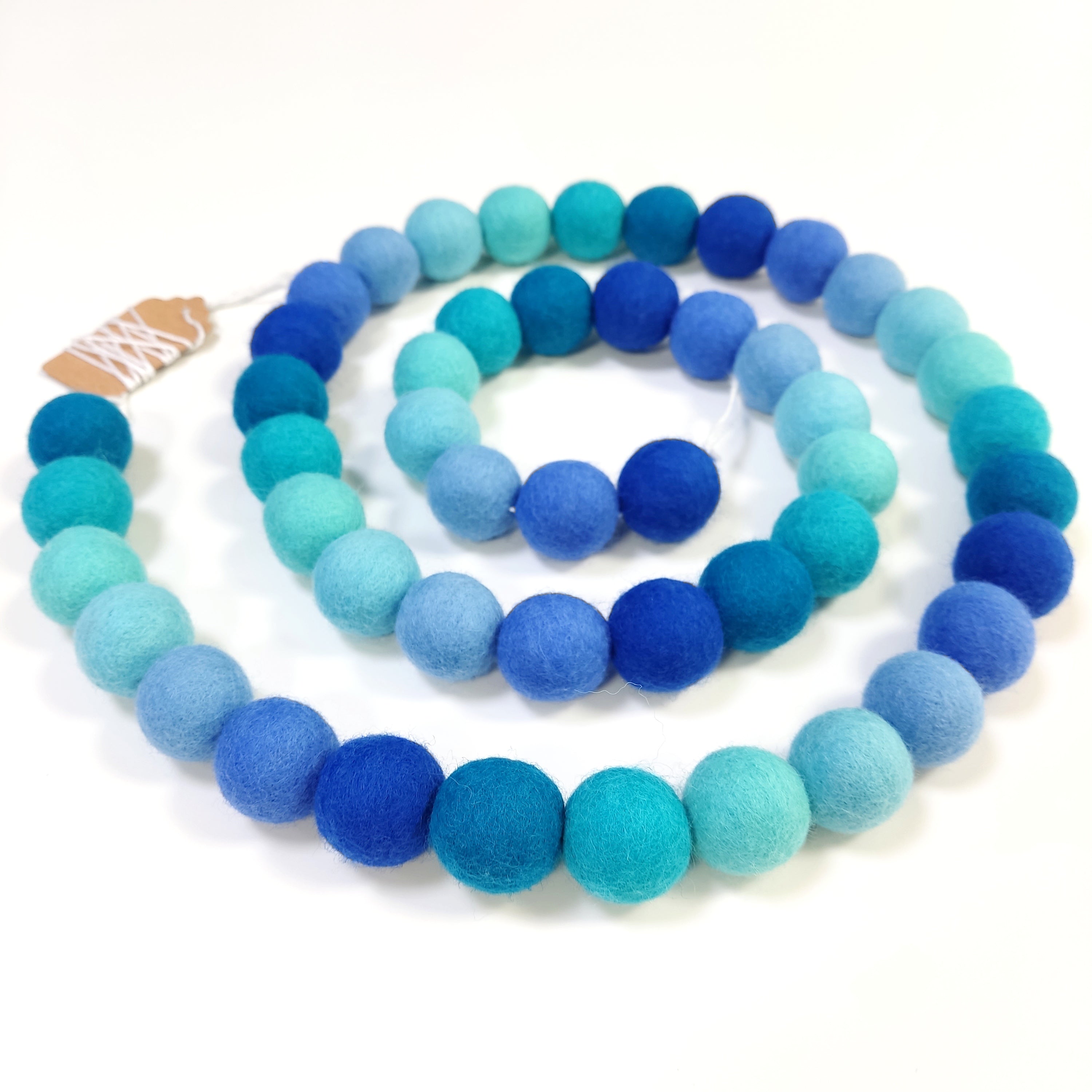 Guirlande de boules de laine feutrée aux teintes bleues disposée en spirale avec les pompons rassemblés sur le fil