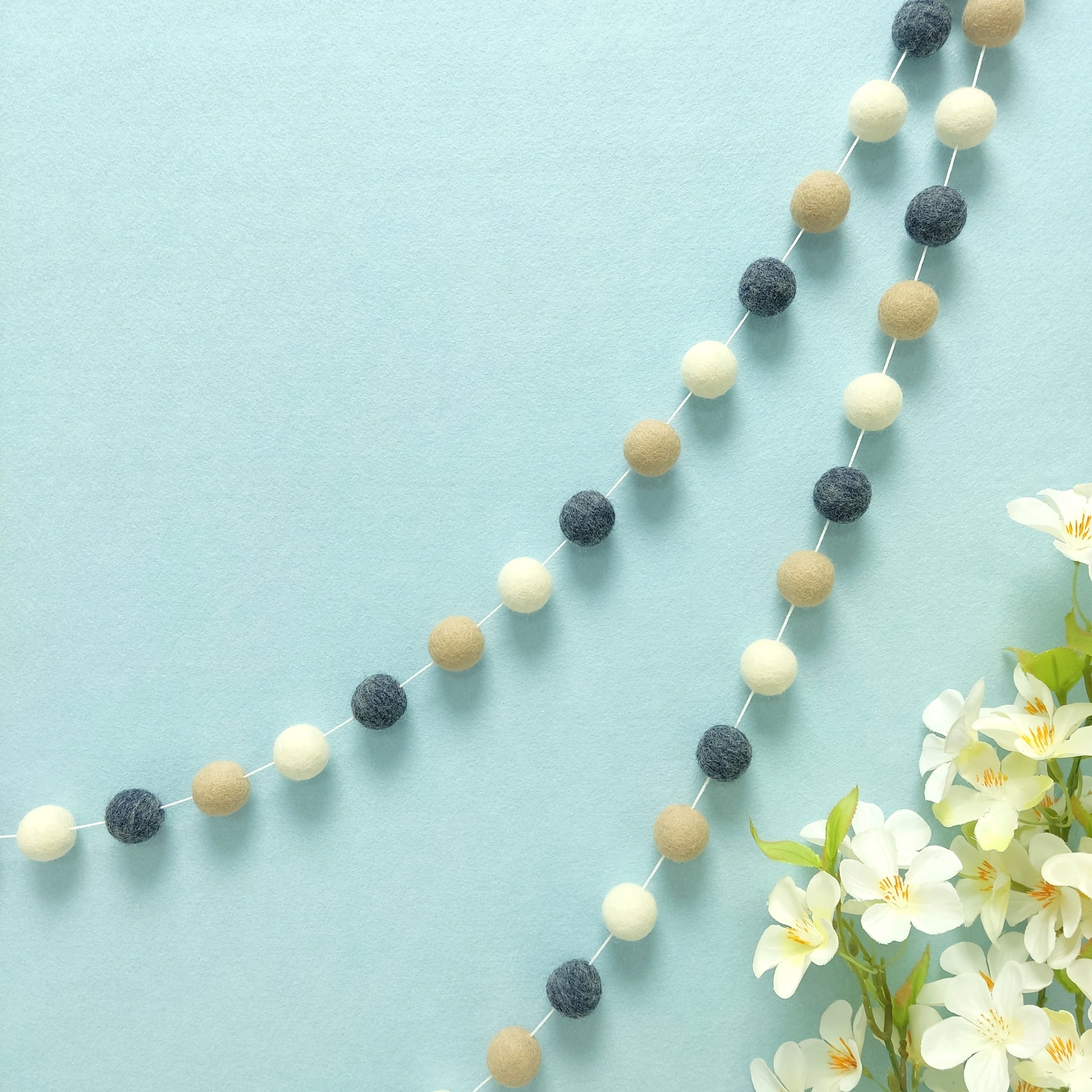 Guirlande en boules de feutre denim beige blanc suspendue sur un mur