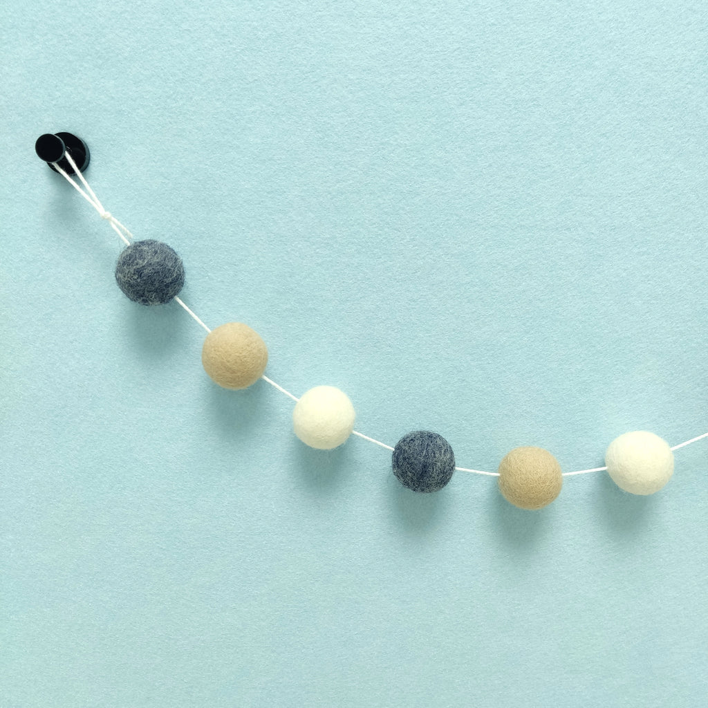 Zoom sur les couleurs de la guirlande de pompons bleu jeans brut, beige poudré et blanc naturel avec la boucle de fixation