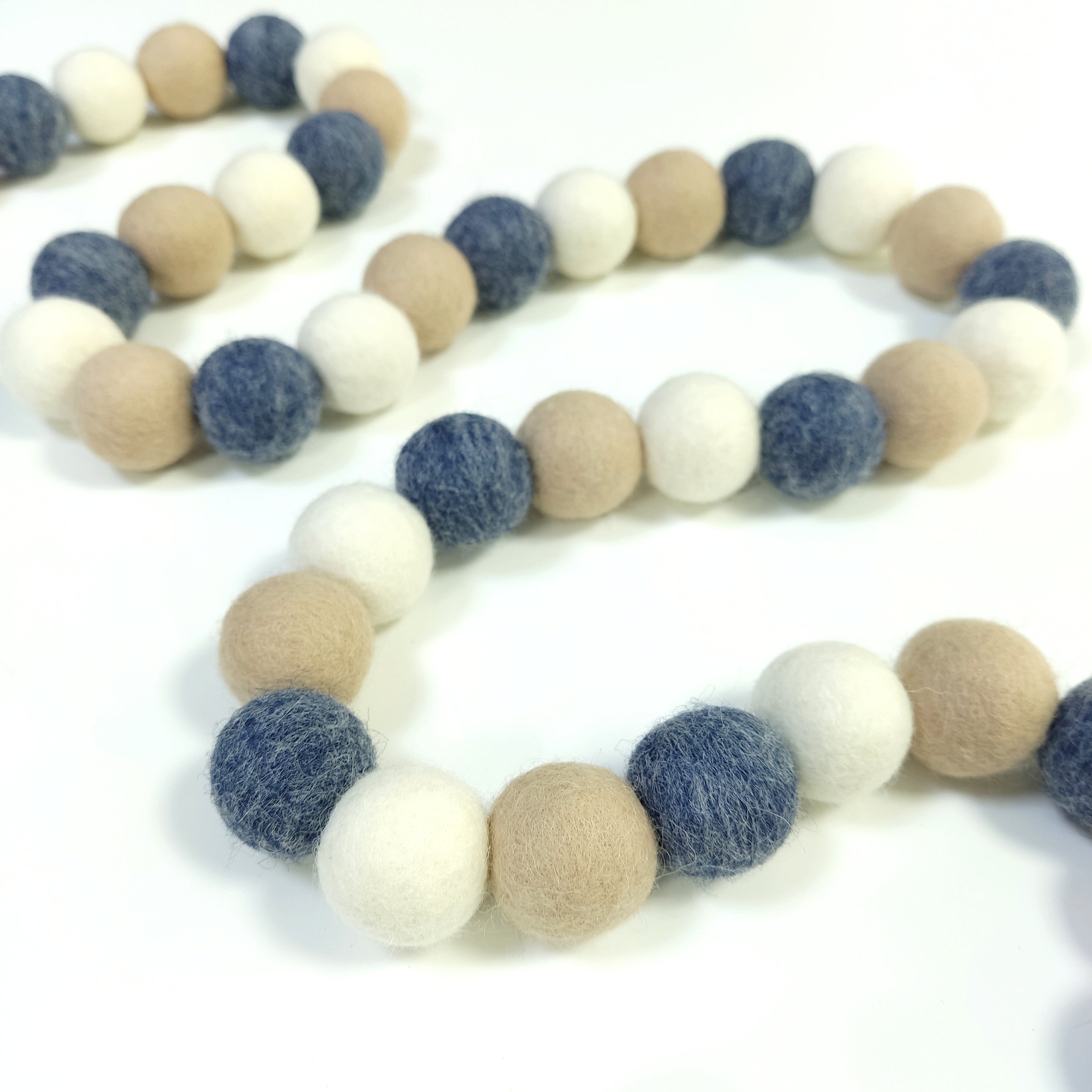 Guirlande denim beige avec ses pompons de feutre rassemblés sur le fil et posée en serpentin sur une table