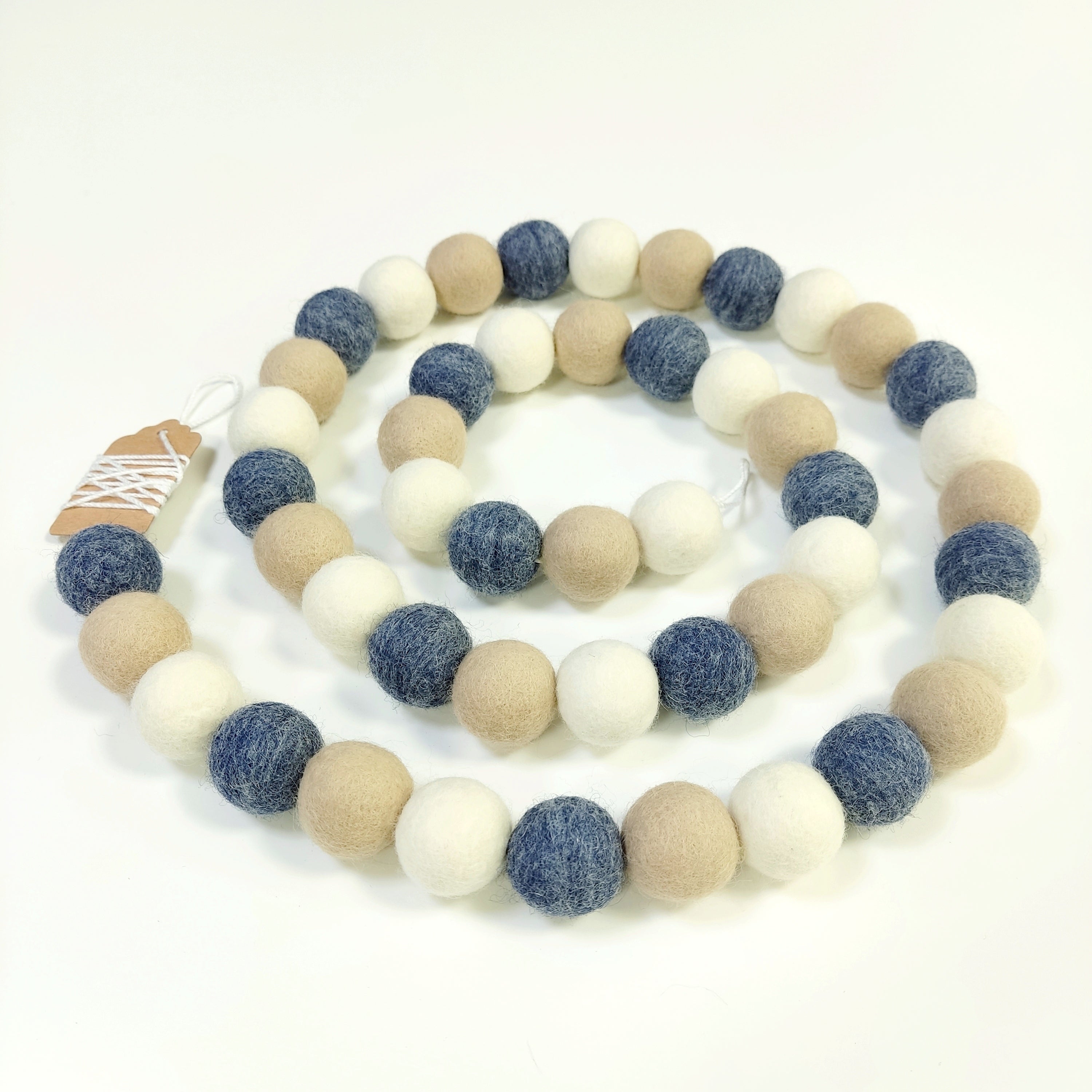 Guirlande en boules de laine feutrée bleu beige et blanc disposée en spirale sur une table
