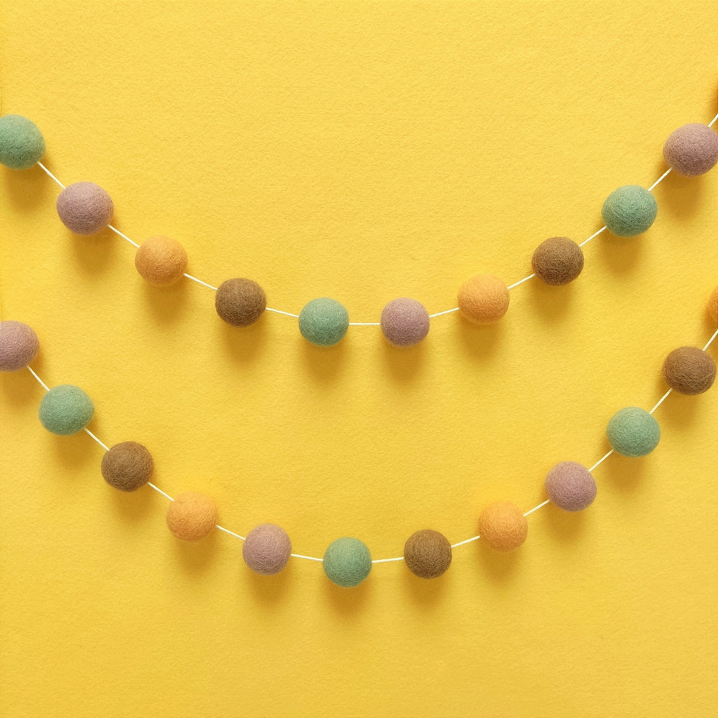 Guirlande de pompons feutrés dolce vita accrochée sur un mur en arc de cercle