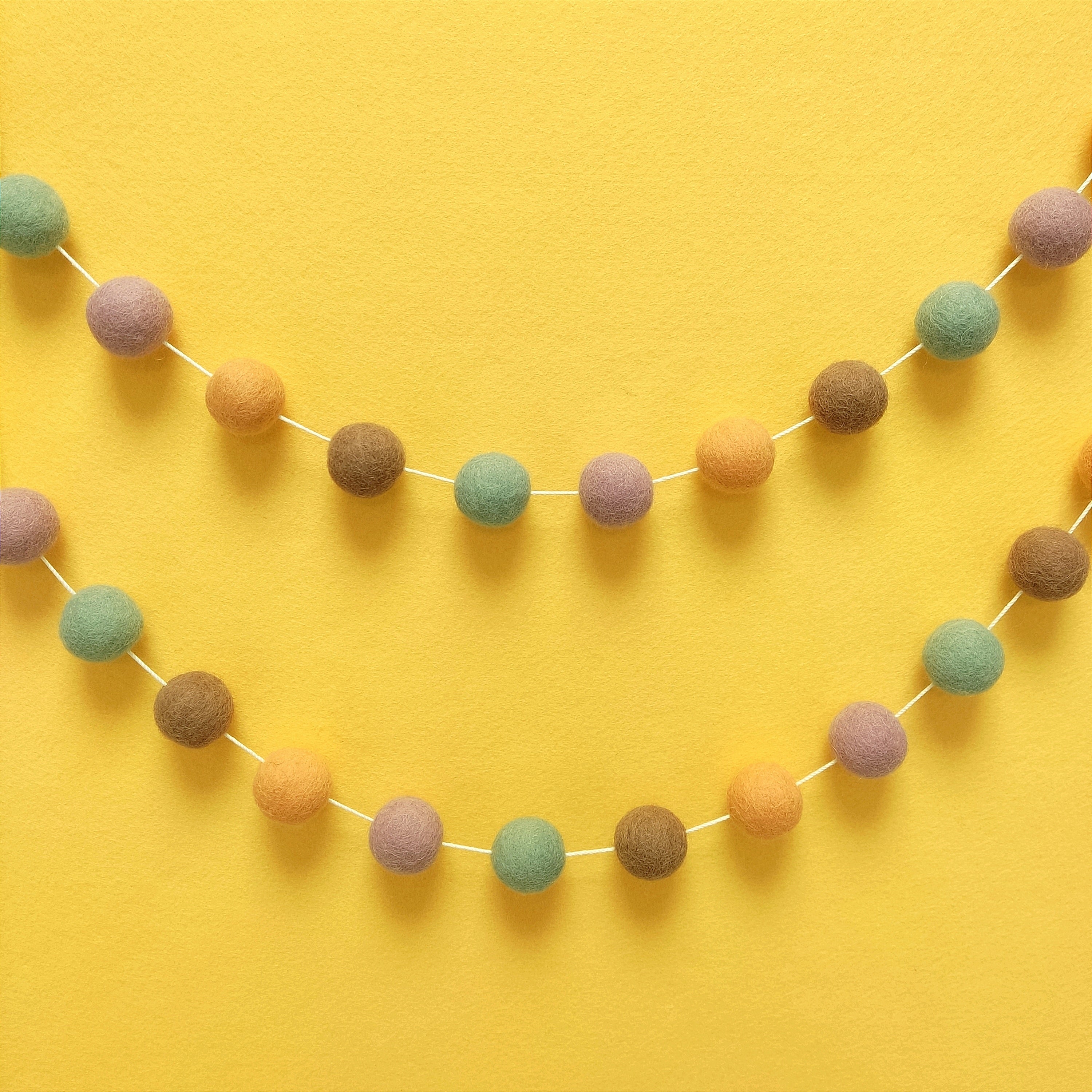 Guirlande de pompons feutrés dolce vita accrochée sur un mur en arc de cercle