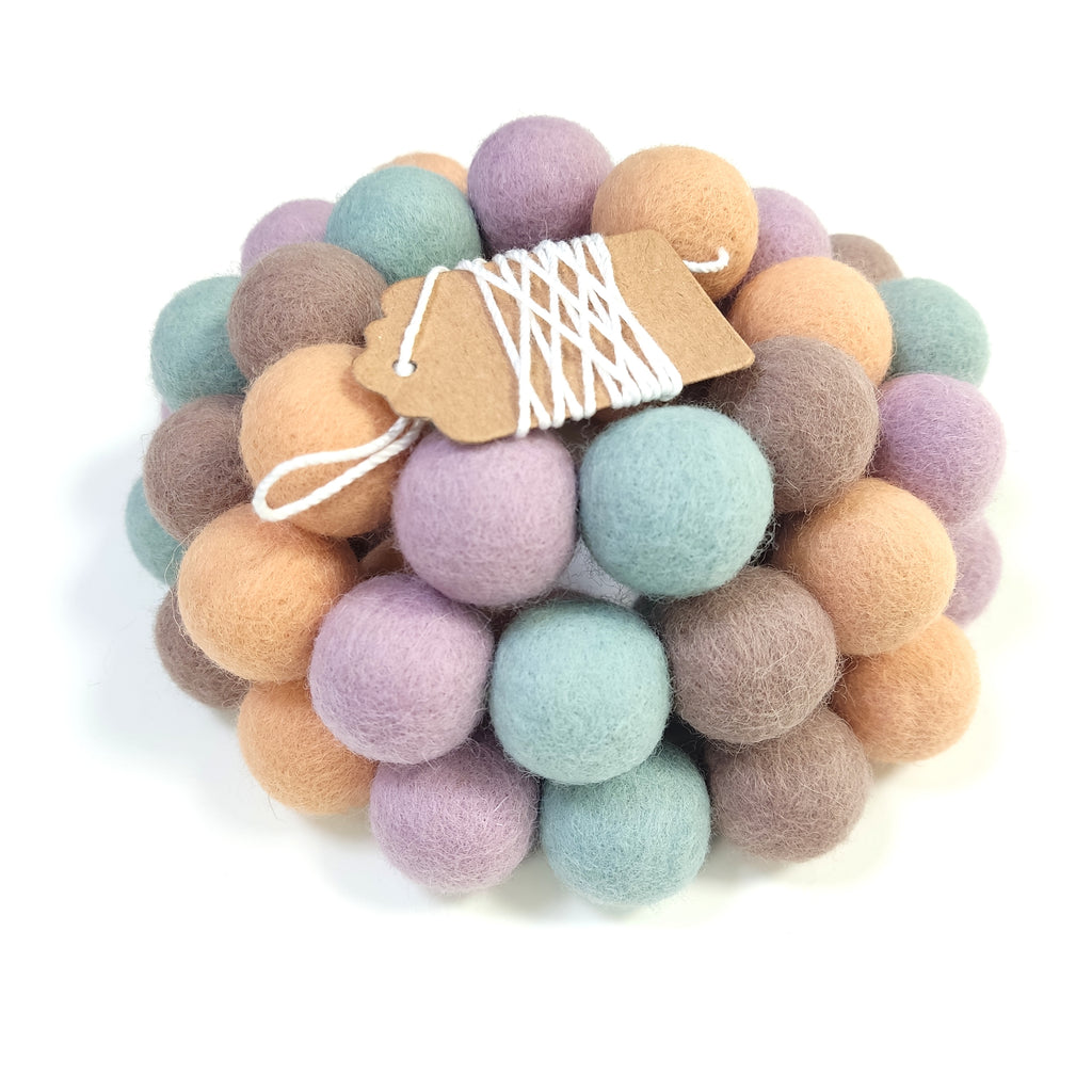 Zoom sur la guirlande de pompons cappuccino, orange pêche, vert céladon et lilas avec son étiquette