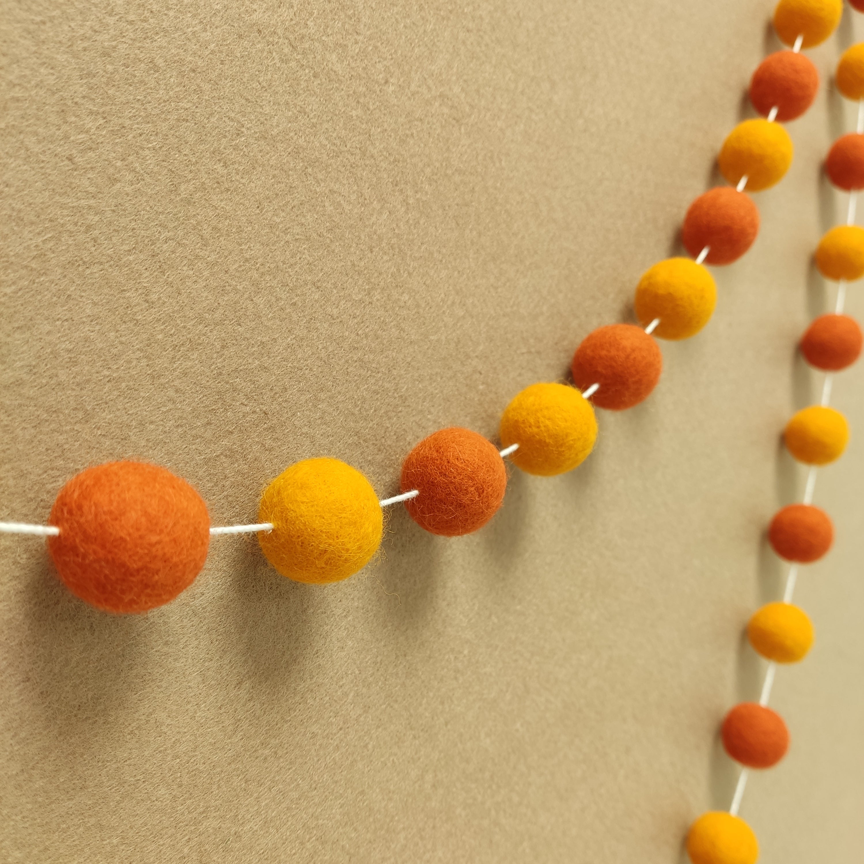 Guirlande de pompons en feutre orange vue de profil sur un mur
