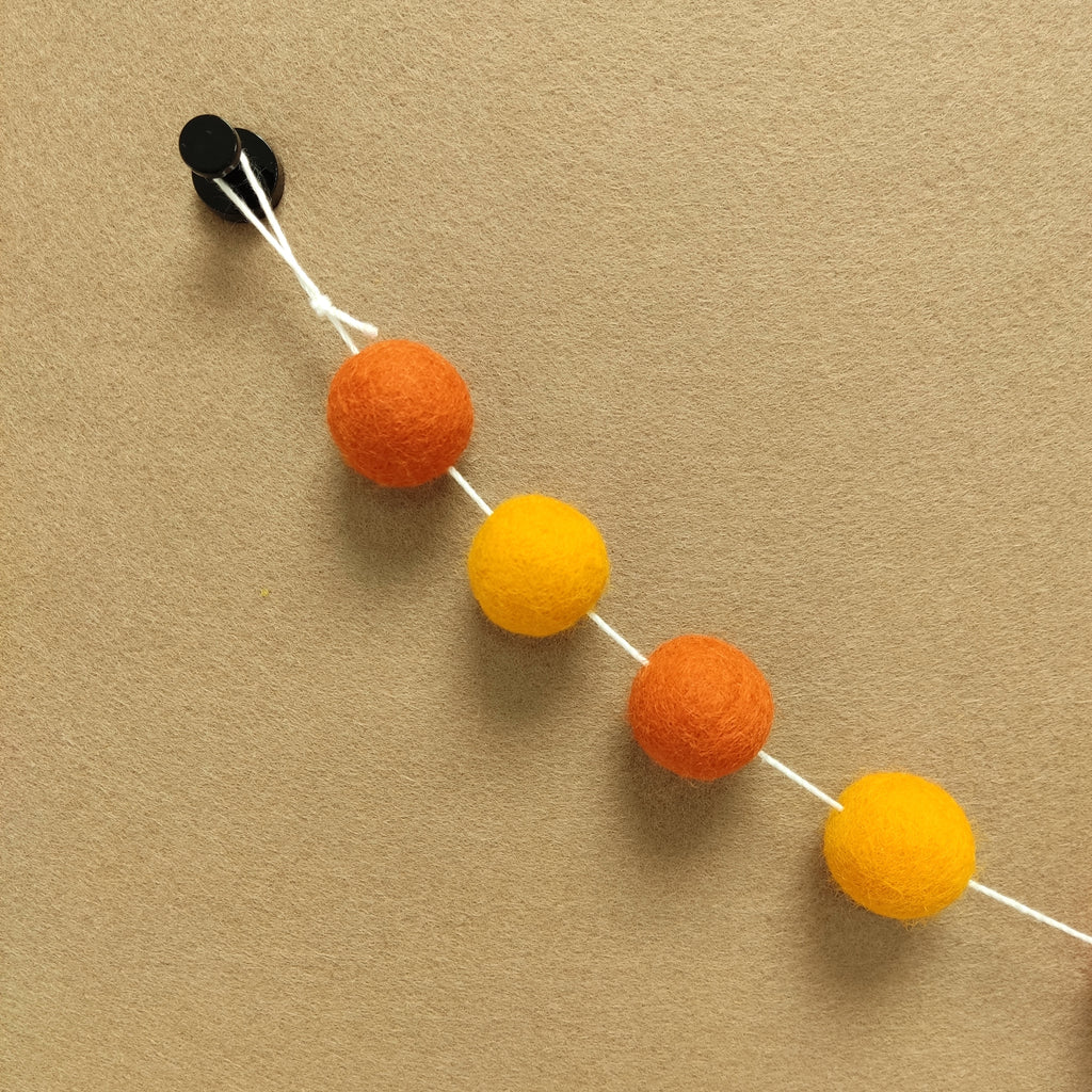 Zoom sur les pompons feutrés orange mandarine et orange marigold de la guirlande duo orange avec la boucle de fixation
