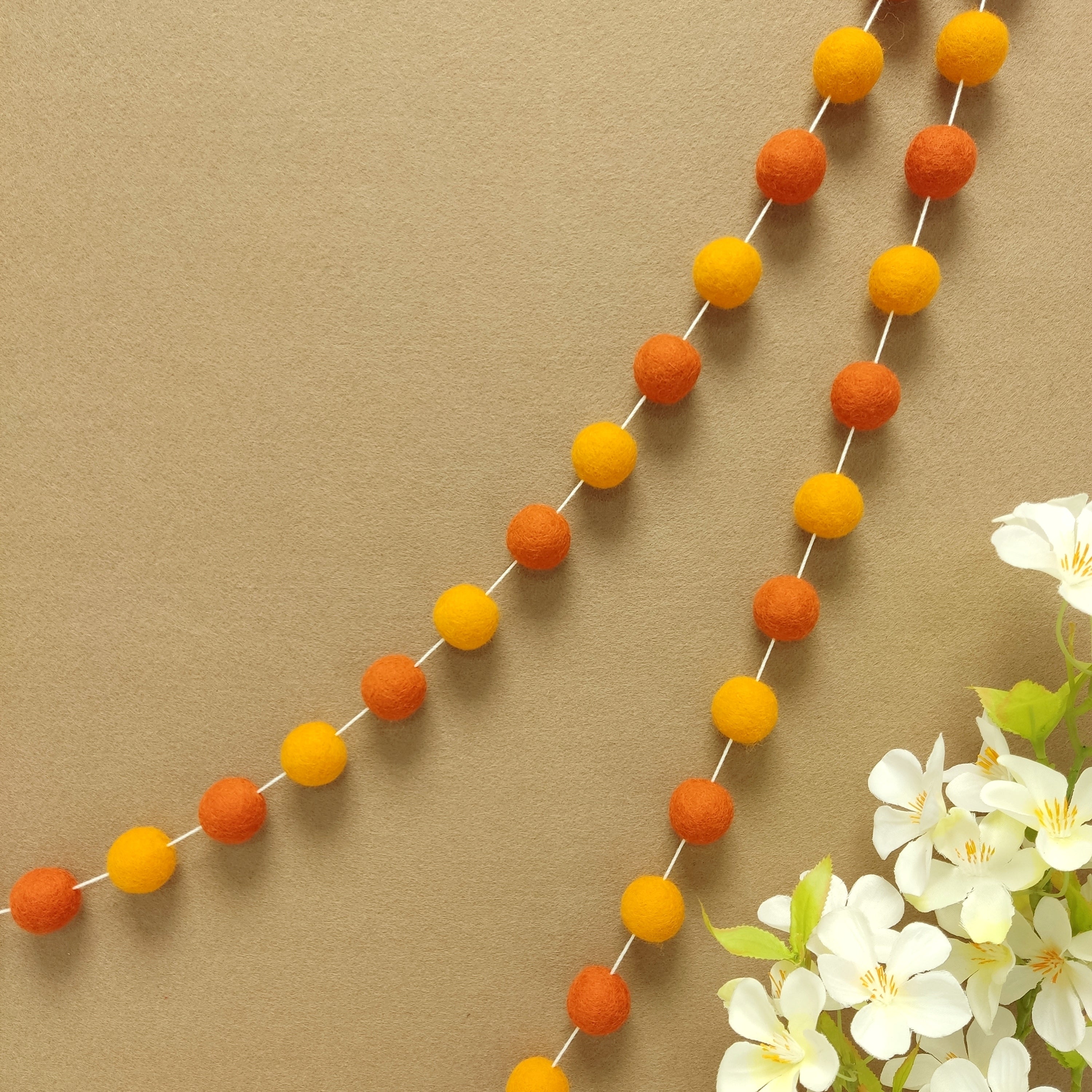 Guirlande en boules de feutre orange mandarine et marigold suspendue sur un mur