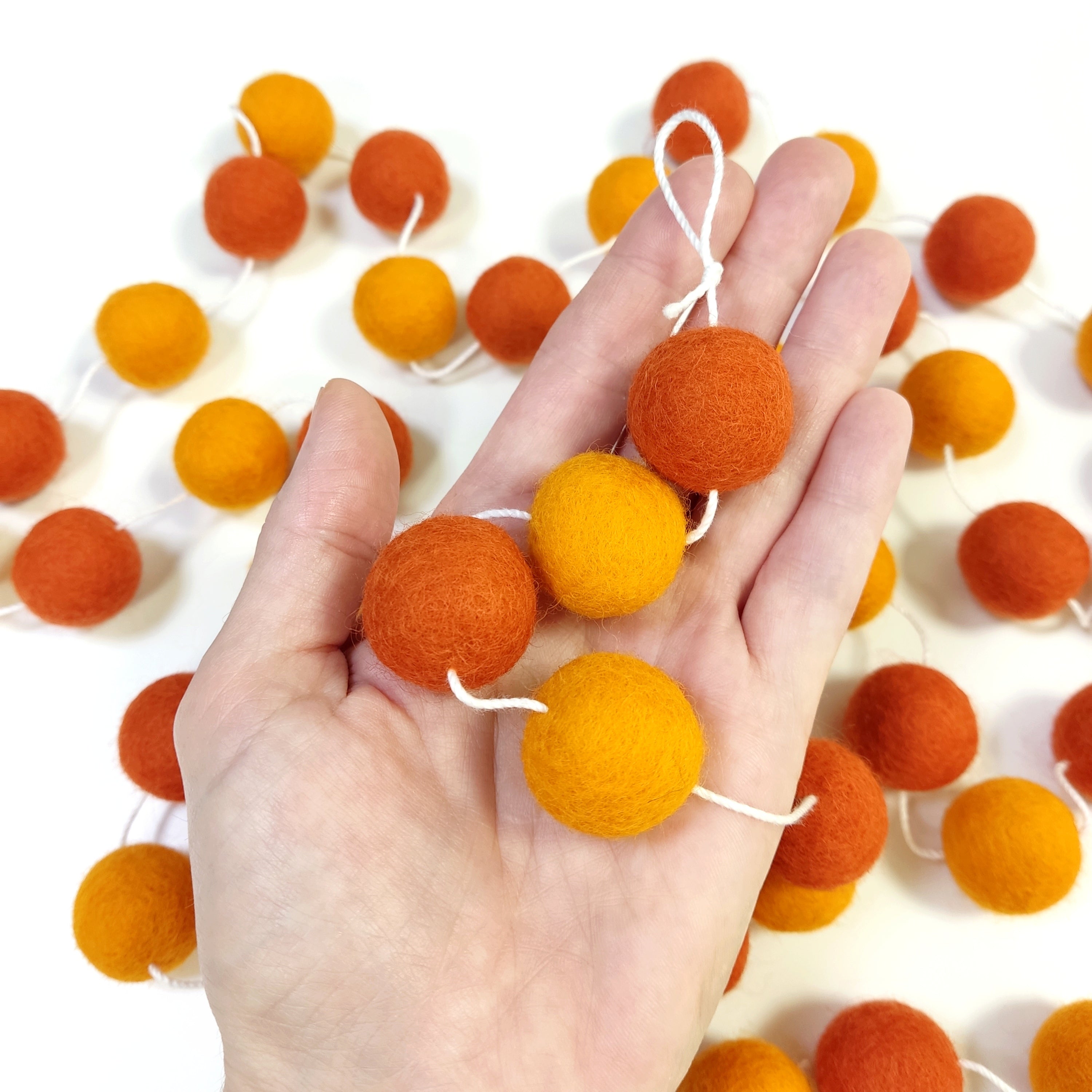 Détail des pompons orange mandarine et marigold dans une main