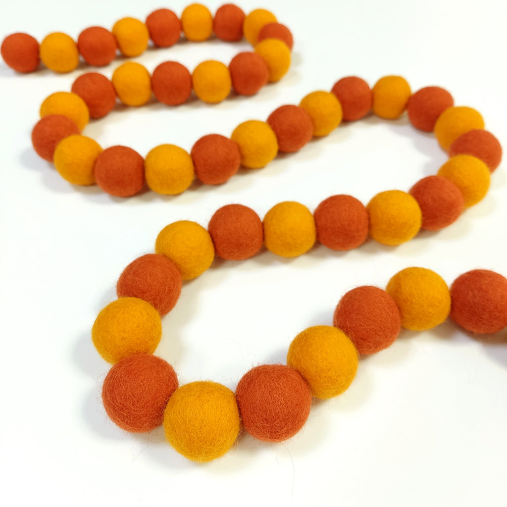Guirlande de pompons orange mandarine et marigold posée en serpentin sur une table