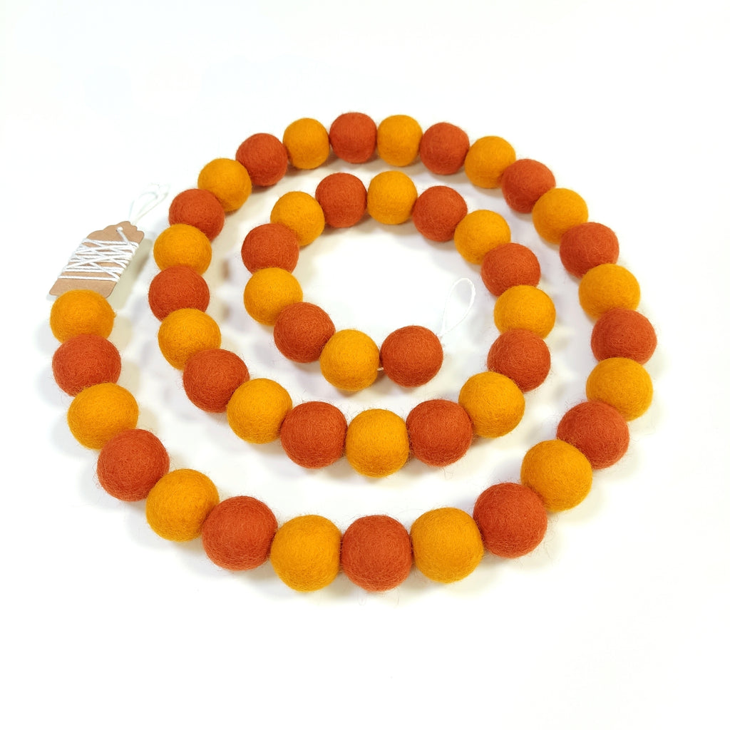 Guirlande en boules de laine feutrée orange mandarine et marigold posée en spirale vue de dessus