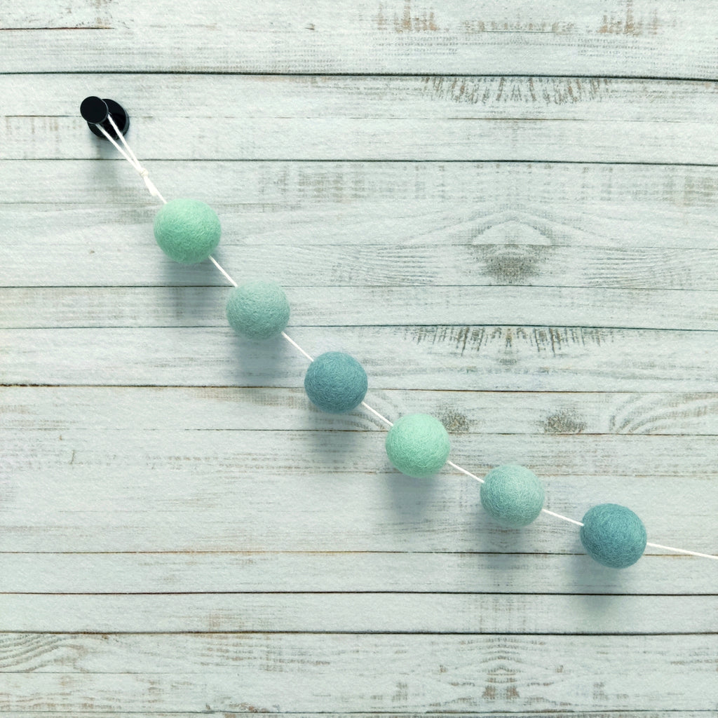 Zoom sur les pompons de feutre vert menthe, vert céladon et bleu nordique de la guirlande eucalyptus en laine mérinos