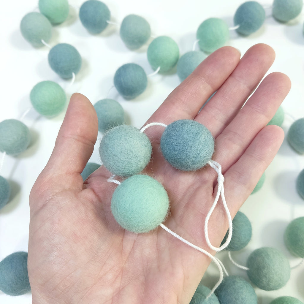 Détail des pompons feutrés de la guirlande eucalyptus dans une main