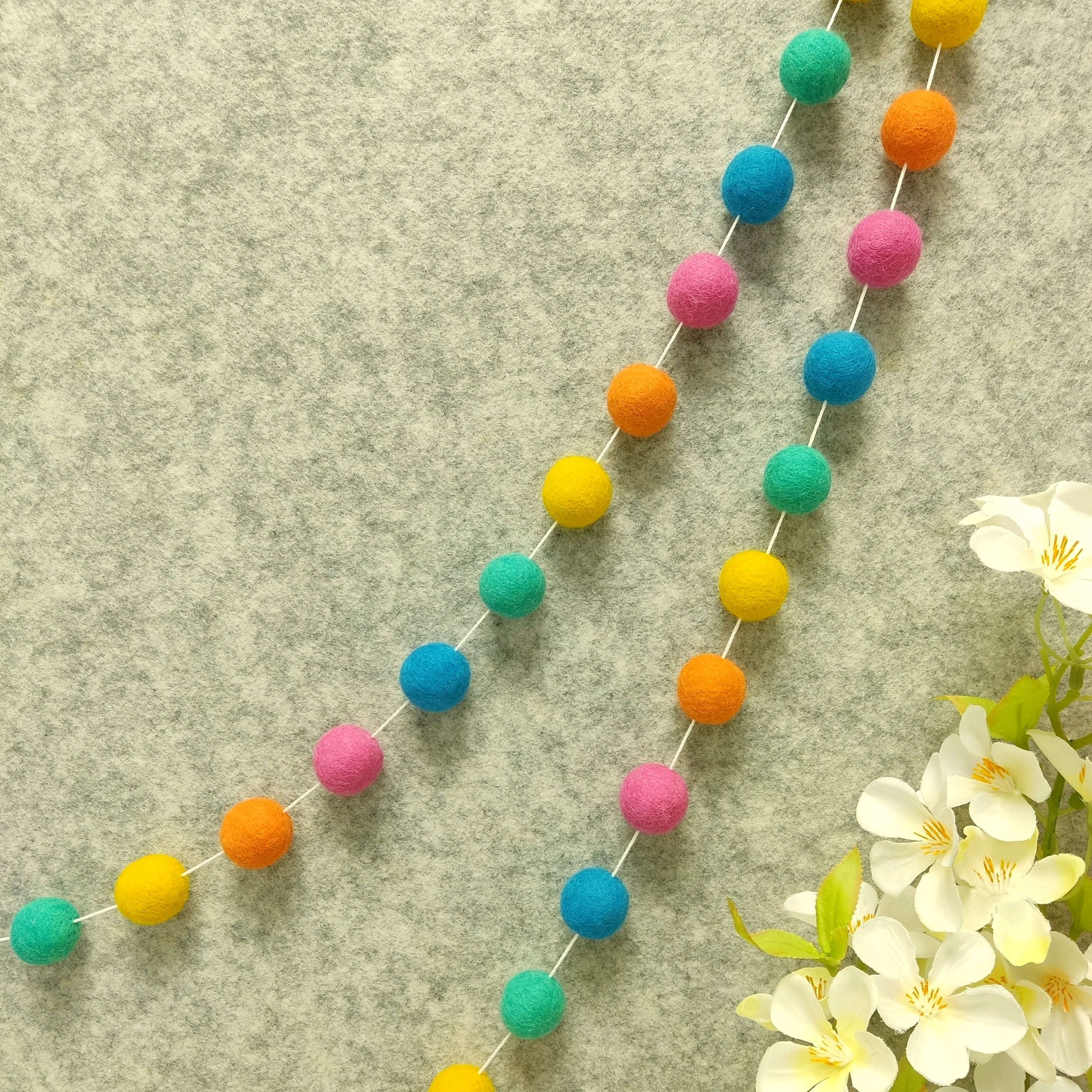 Guirlande de pompons feutrés aux couleurs flashy rose vert jaune bleu orange suspendue sur un mur