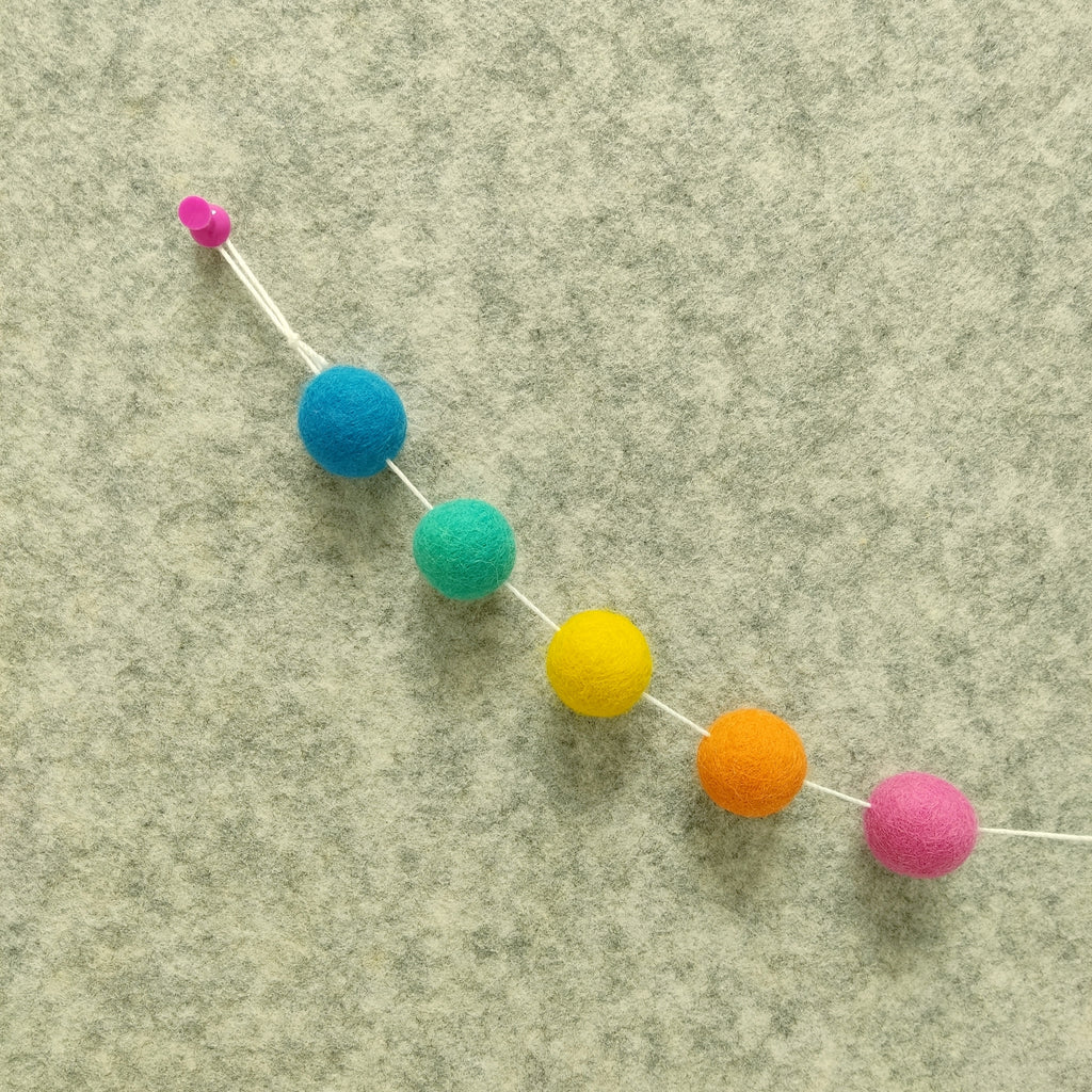 Zoom sur les couleurs jaune soleil, rose bonbon, orange carotte, vert lag et bleu océan de la guirlande de pompons flashyn