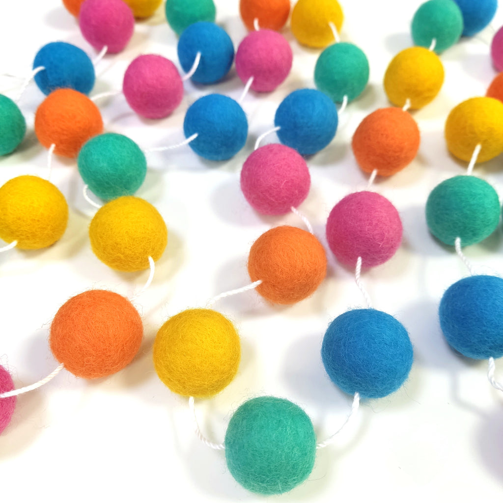 Guirlande de pompons en laine feutrée flashy étalée sur une table