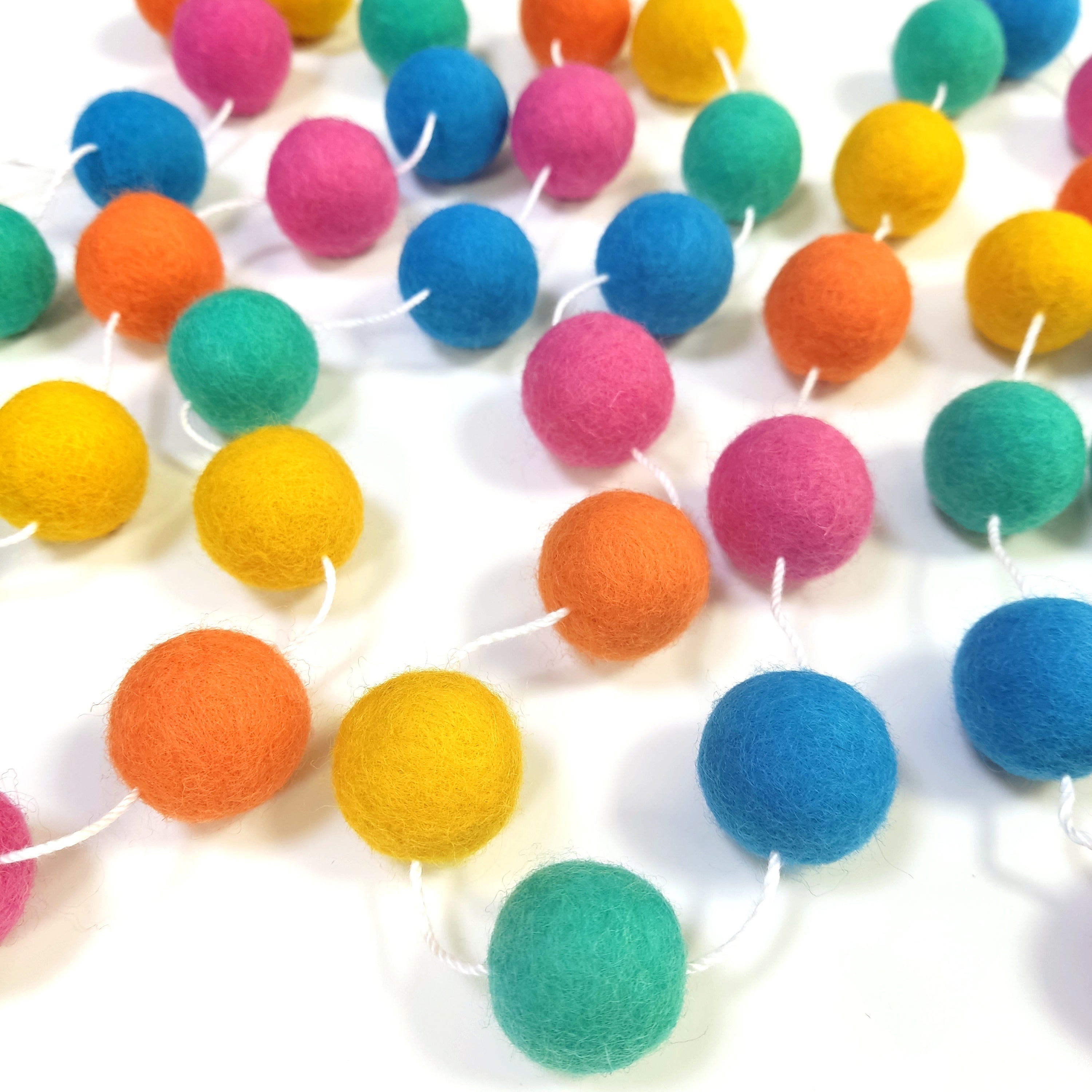 Guirlande de pompons en laine feutrée flashy étalée sur une table