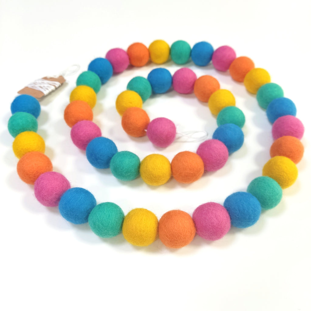 Guirlande de boules de laine feutrée rose orange jaune lagon bleu disposée en spirale vue de dessus