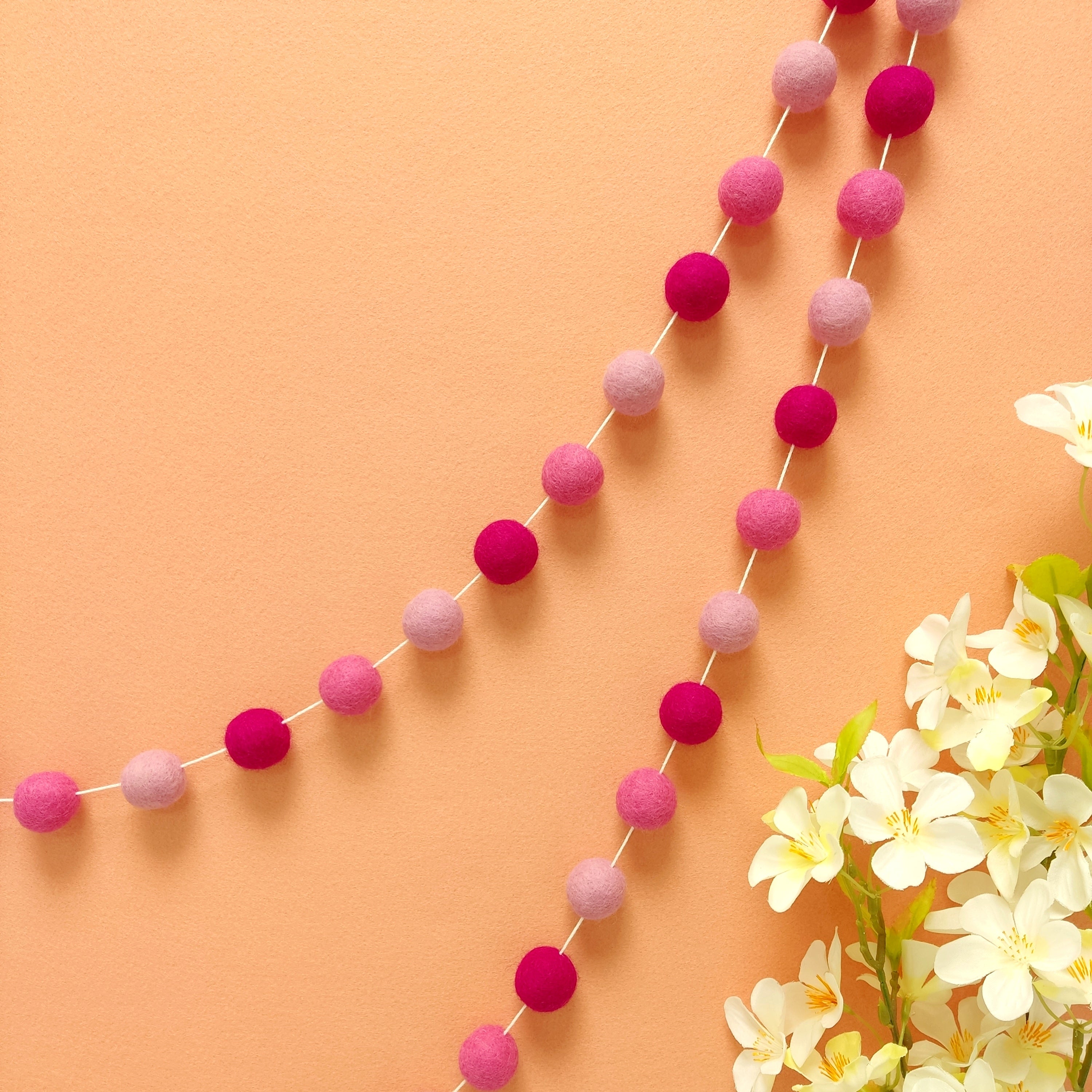 Guirlande de pompons feutrés en laine mérinos rose magenta, rose bonbon et rose cerisier accroché sur un mur