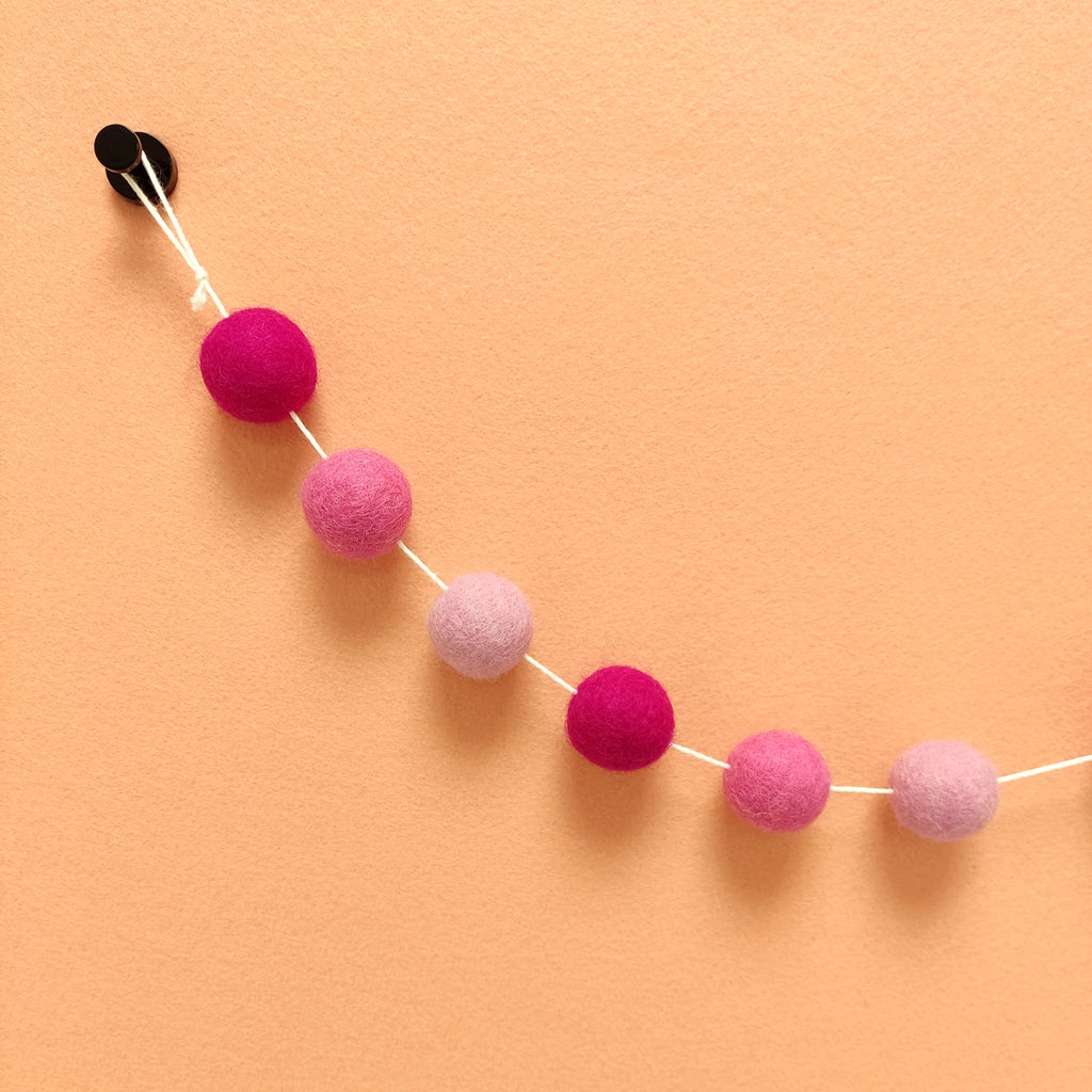 Détail des pompons de feutre rose magenta, rose bonbon et rose clair de la guirlande fleurs de cerisier sur le fil avec sa boucle de fixation